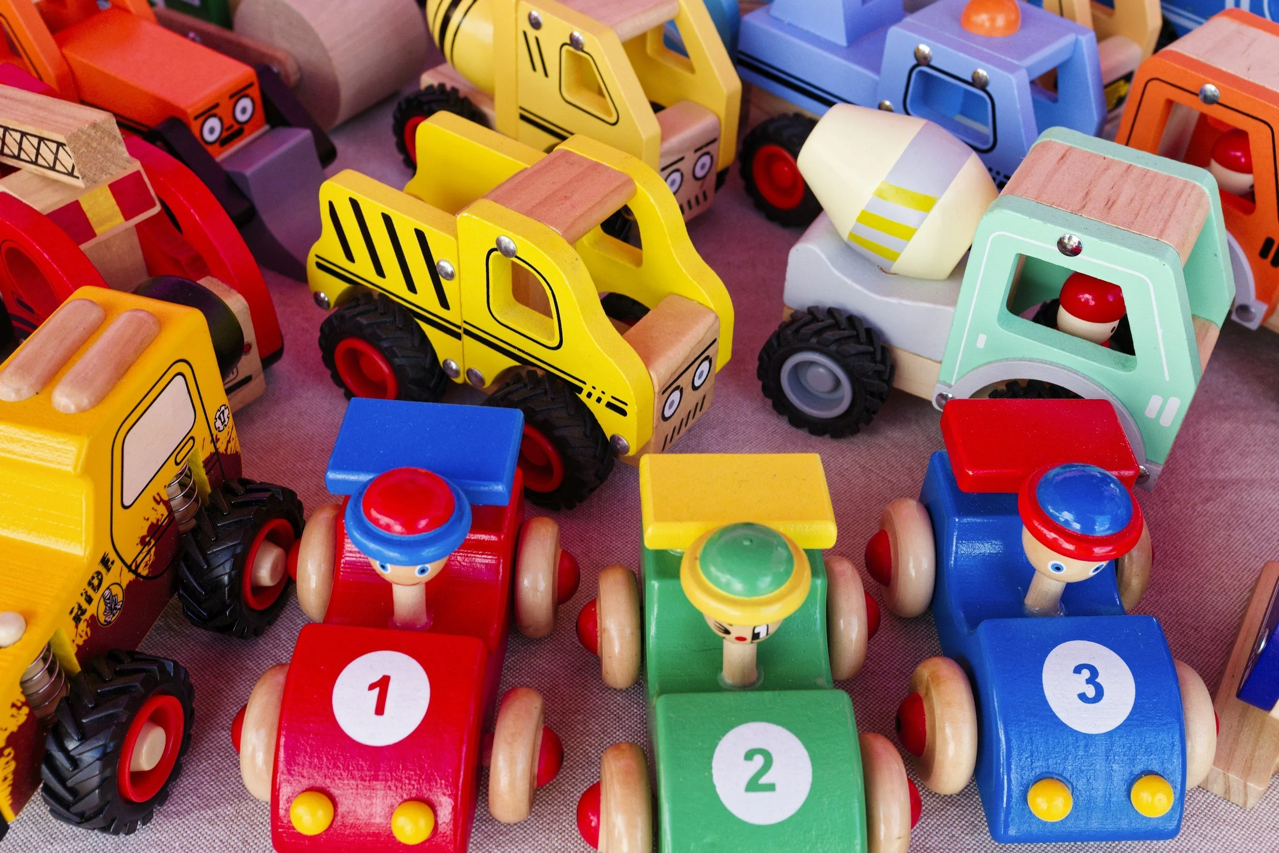 Colorful wooden toy vehicles including race cars with driver figures and construction trucks on display.