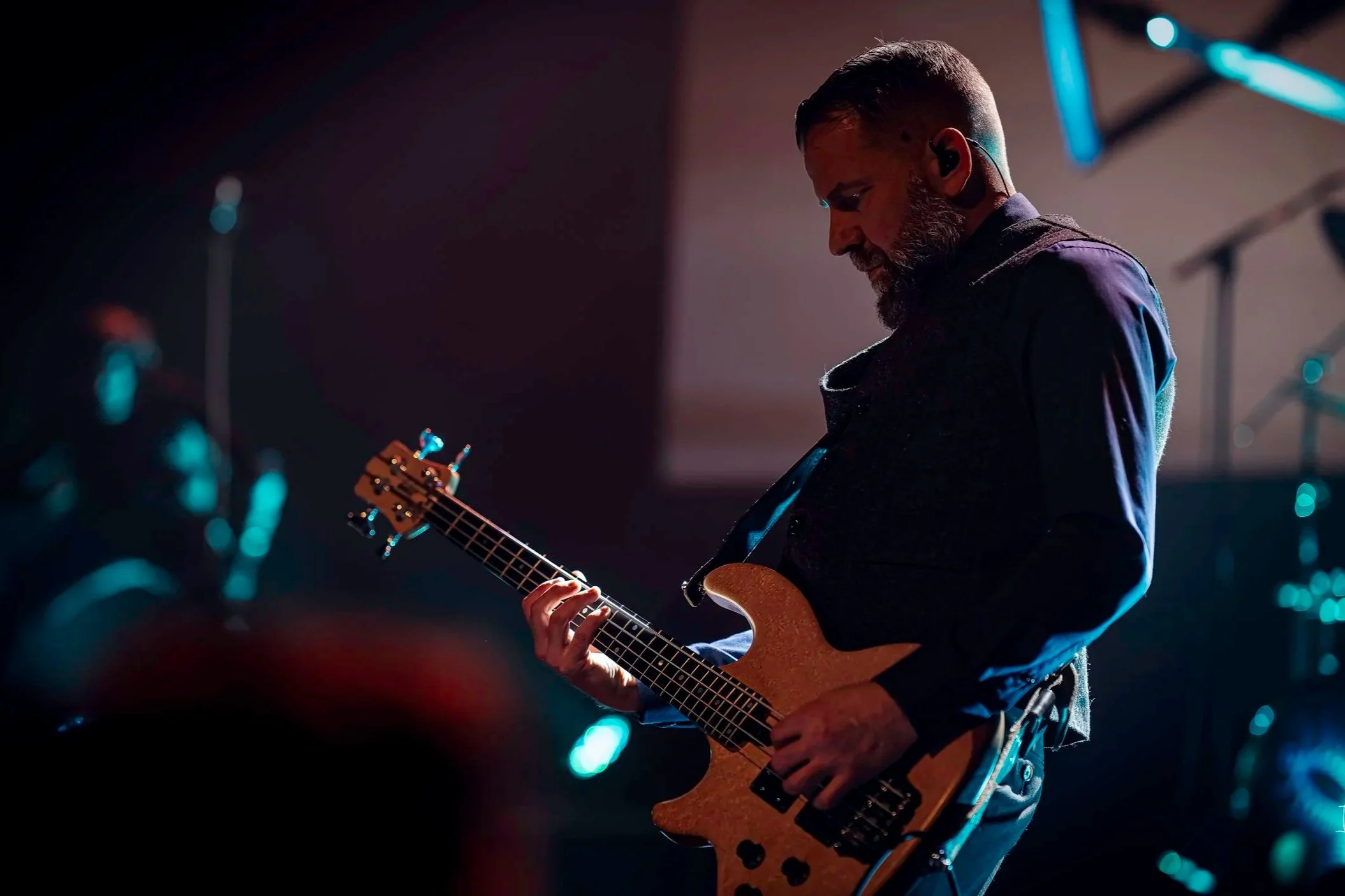 Musician playing an electric bass guitar on stage under dim lighting.