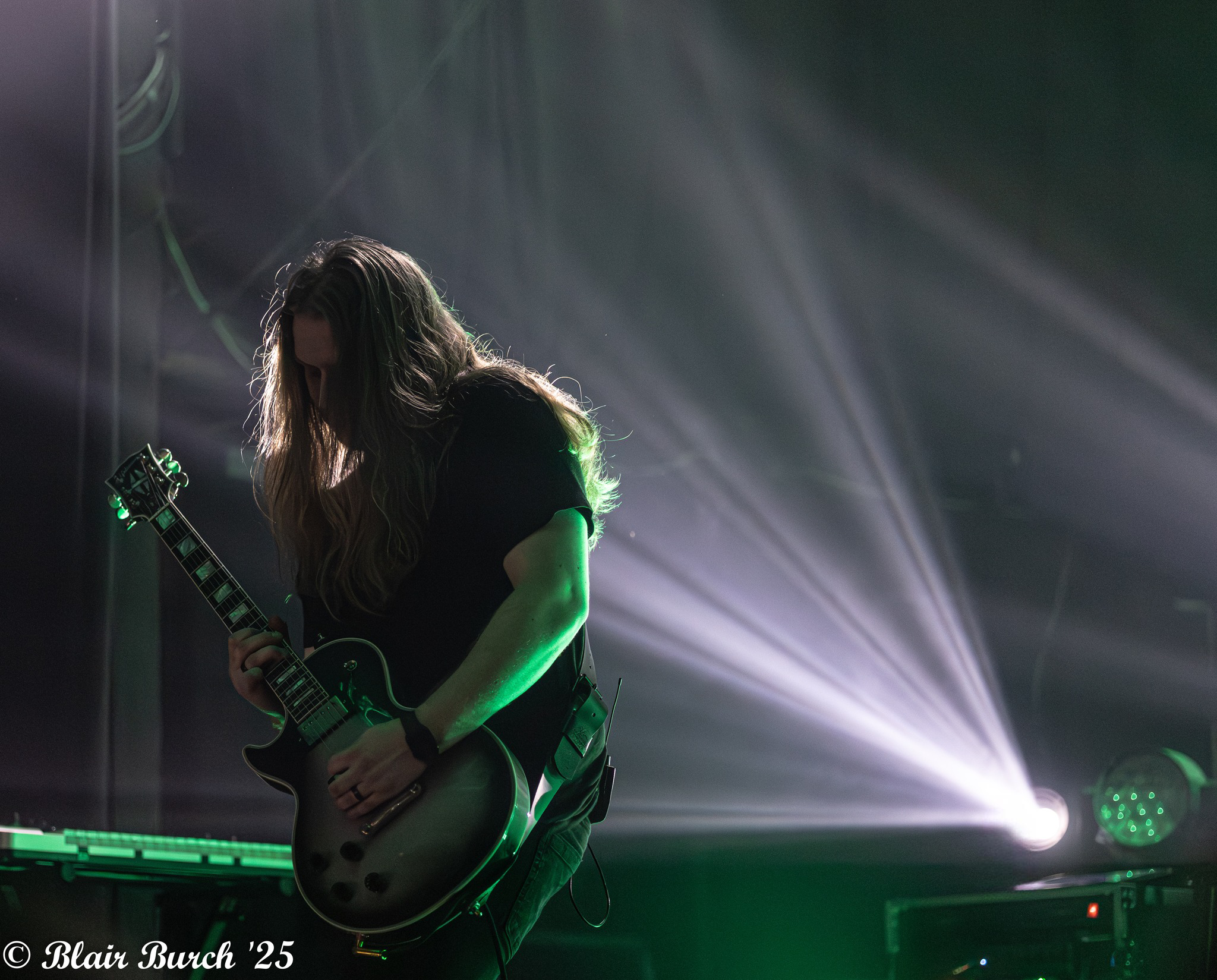 A female guitarist performing on stage with green lighting and fog effects.