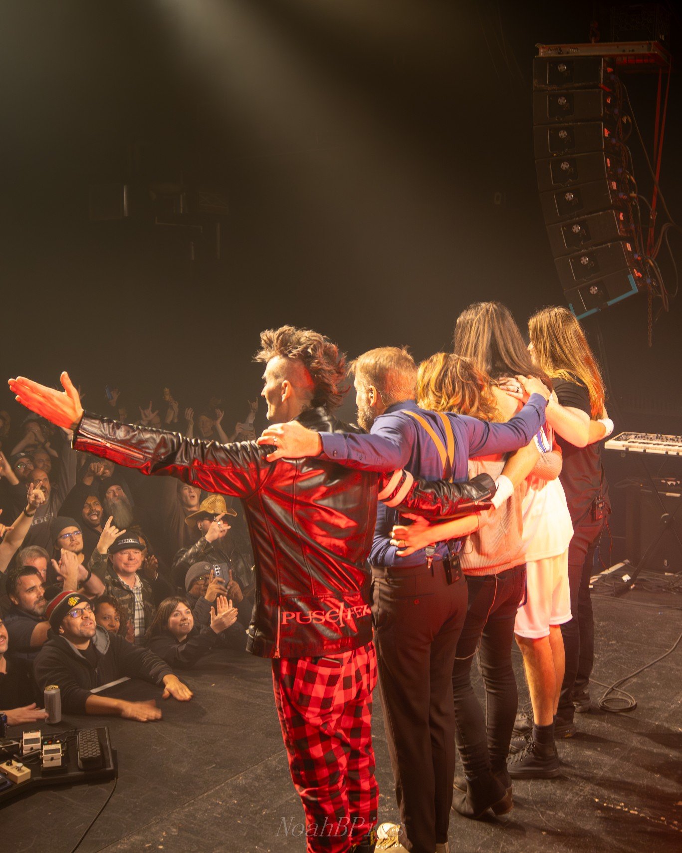 Group of performers on stage embracing and taking a bow in front of an audience in a concert setting.