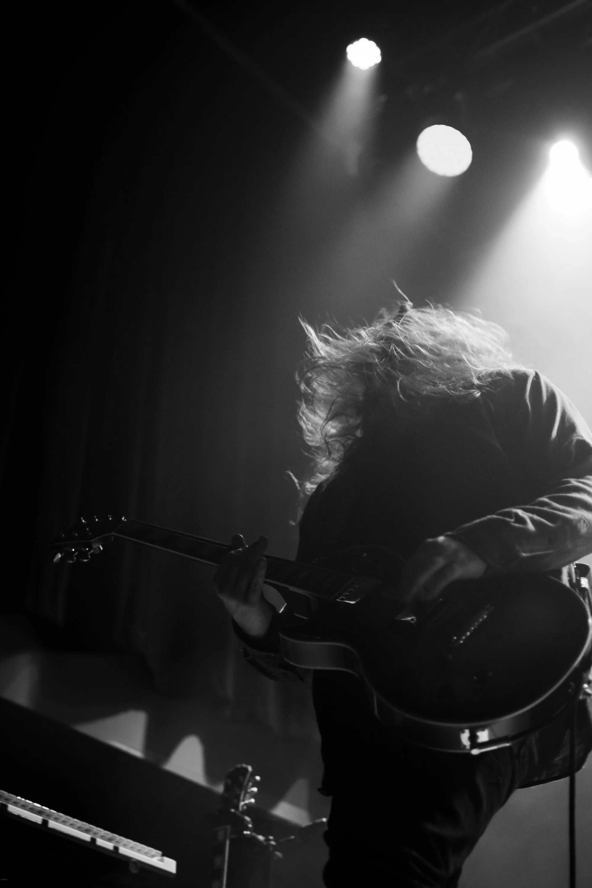 A musician playing an electric guitar on stage with spotlights overhead, black-and-white photo, silhouette and motion.
