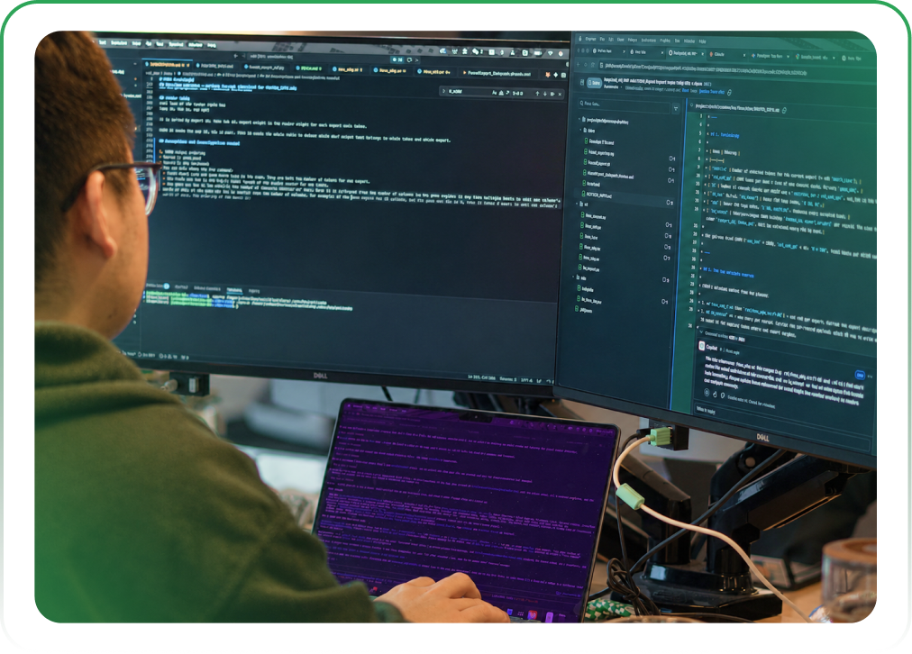 Person working at a desk with multiple computer monitors displaying lines of code and a laptop with terminal output.