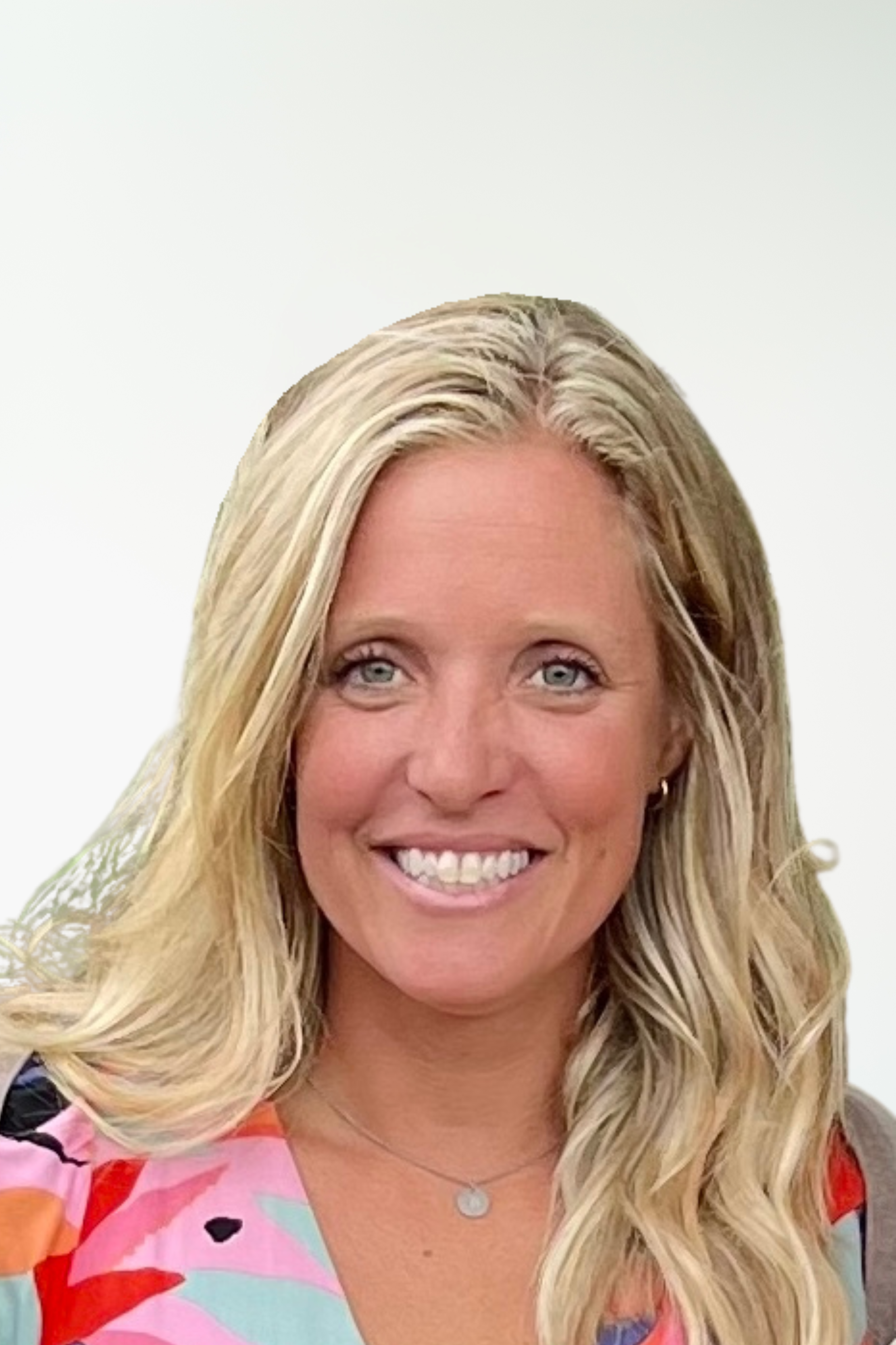 Close-up of a smiling woman with long blonde hair wearing a colorful dress with pink, red, orange, and black patterns, and a silver necklace with a round pendant.