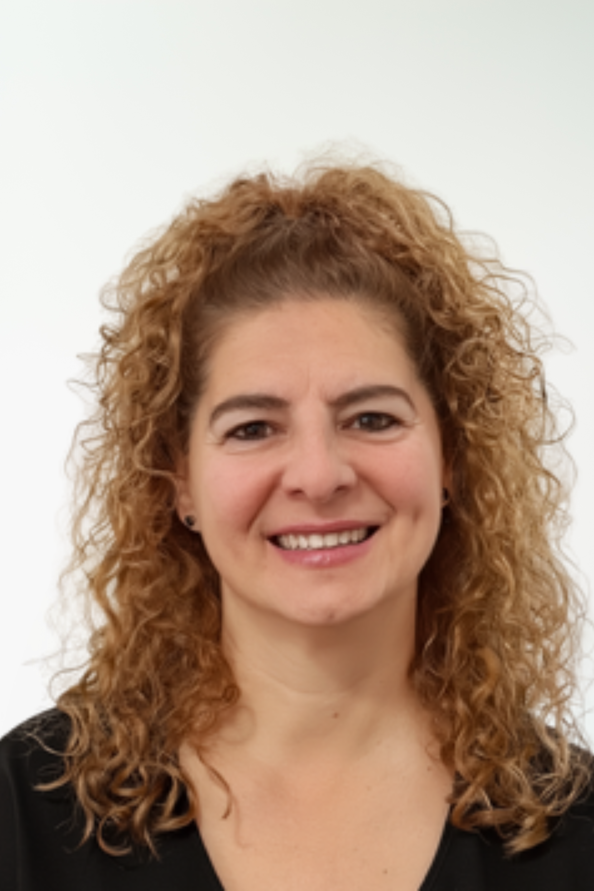 A woman with curly red hair and a black top, smiling against a plain white background.