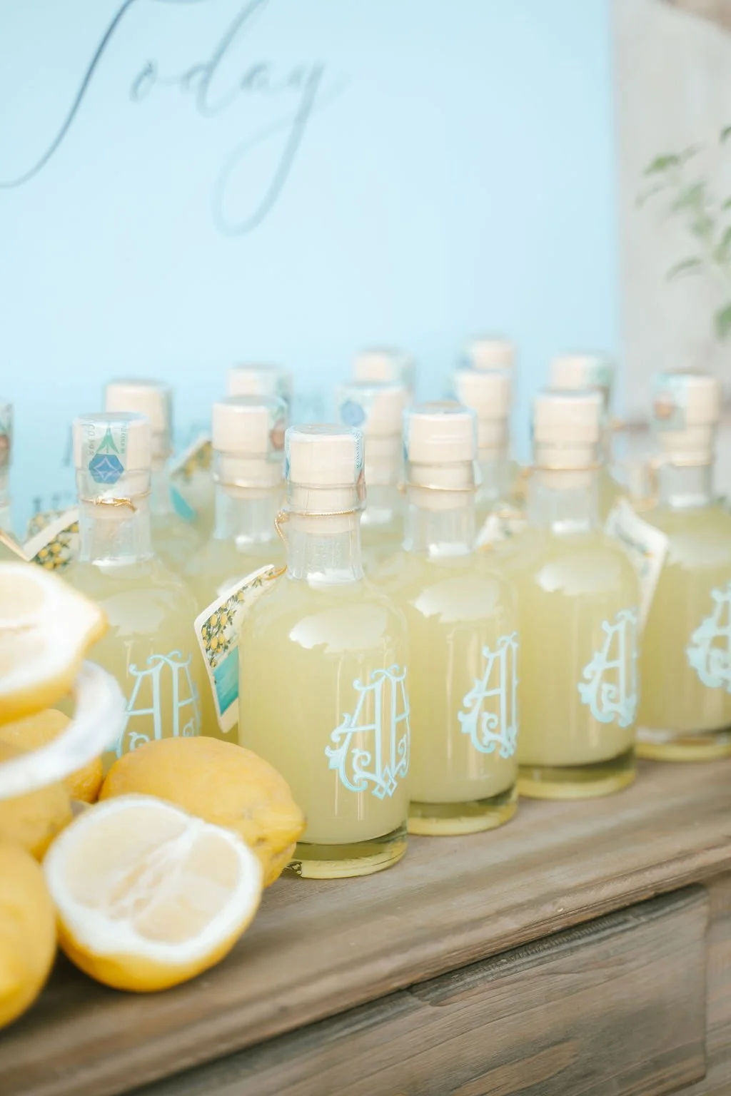 Bottles of lemon-flavored drink with monogrammed labels, lemons, and cut lemon slices on a wooden surface.