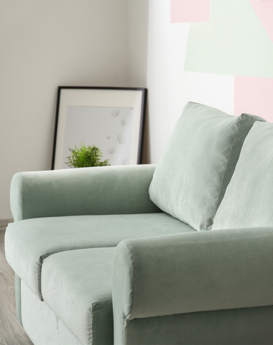 Light green sofa in a room with framed artwork and a potted plant against a decorated wall.