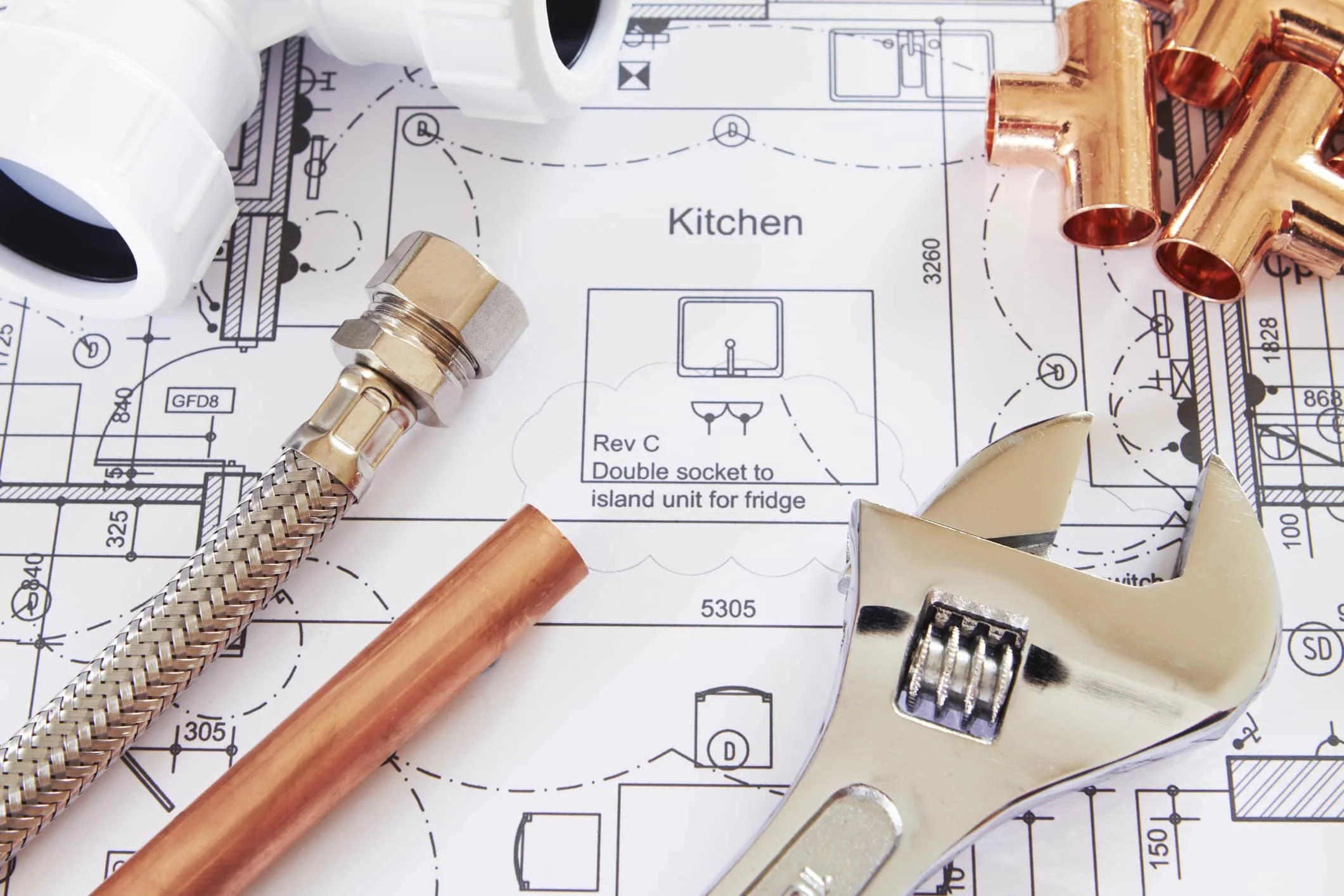 Tools including copper pipe fittings, a braided metal hose, and a pipe cutter lying on a blueprint of a kitchen plumbing plan.