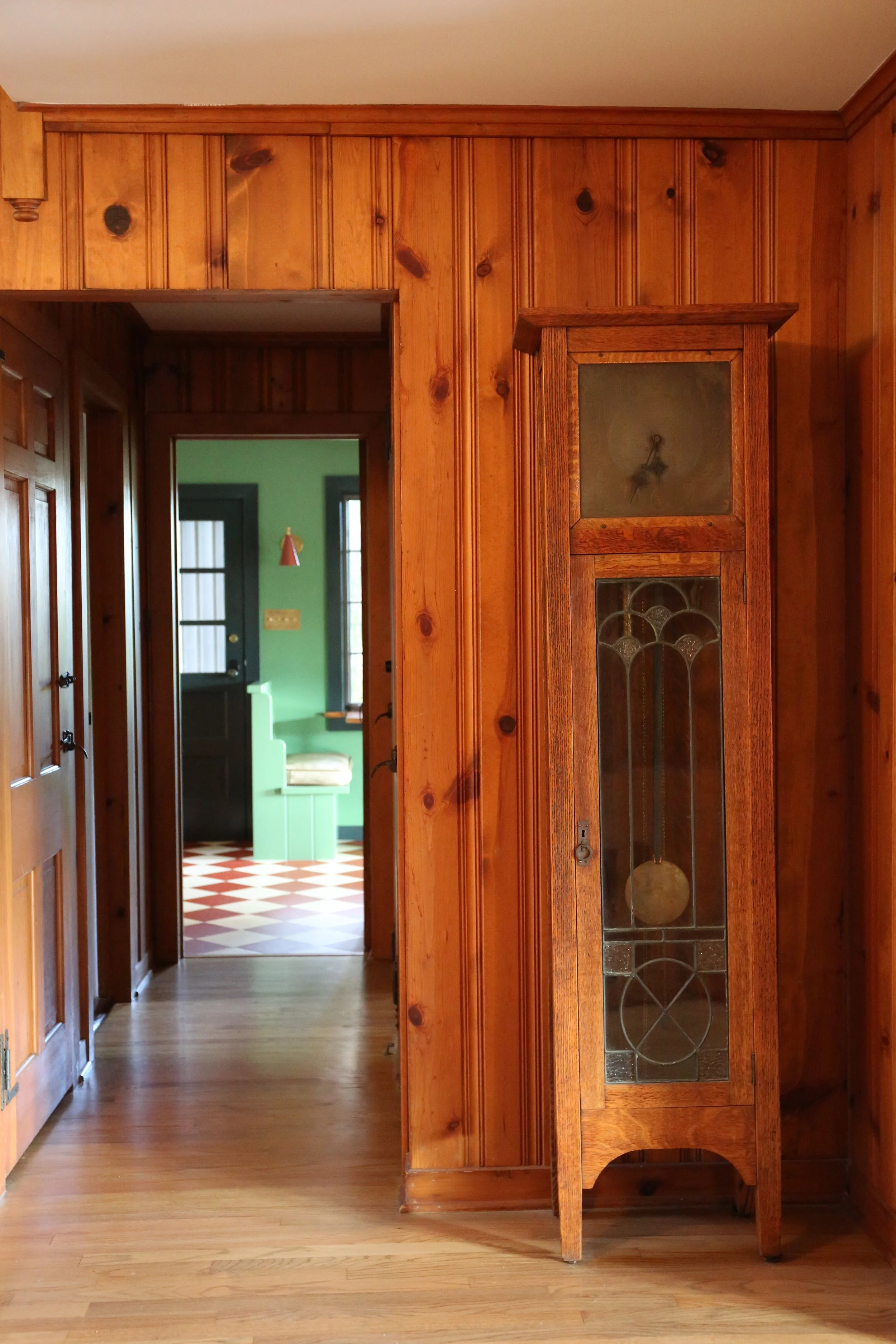 Wooden interior with an antique grandfather clock, hallway view into kitchen.