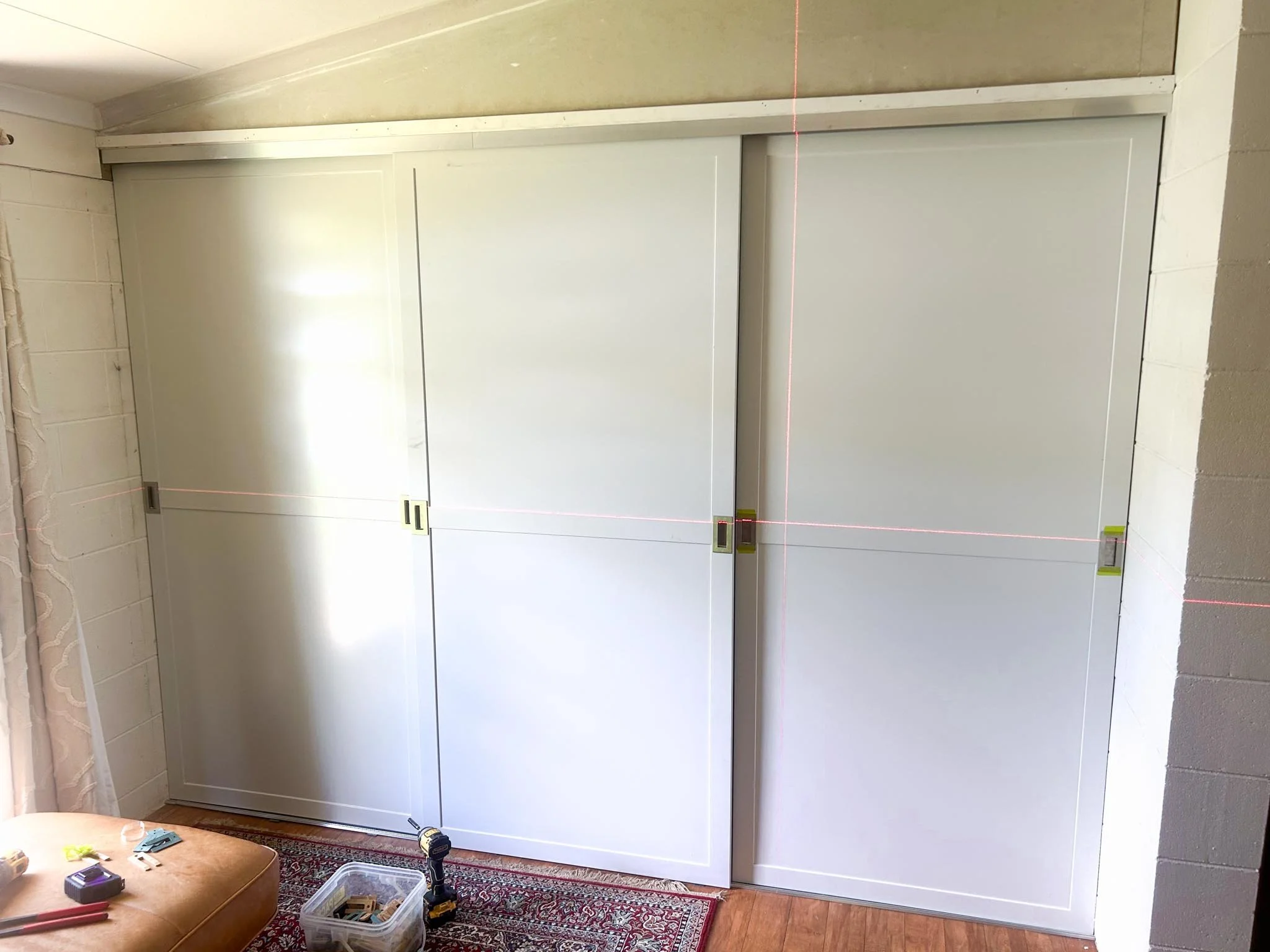 White sliding closet doors in a room with tools and a power drill on the floor nearby.