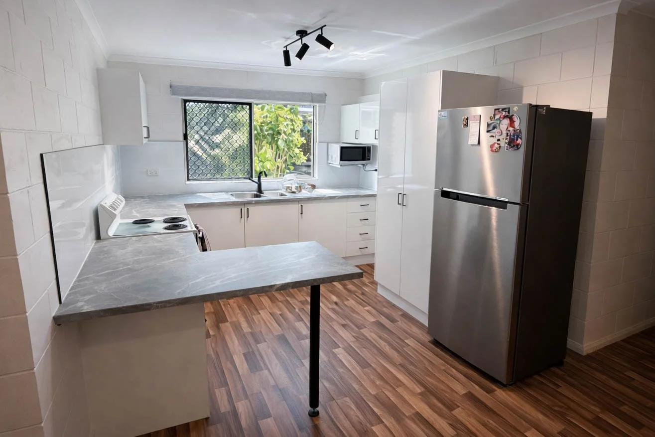 Kitchen with white cabinets, microwave, refrigerator with magnets, stove, and a window showing greenery outside.