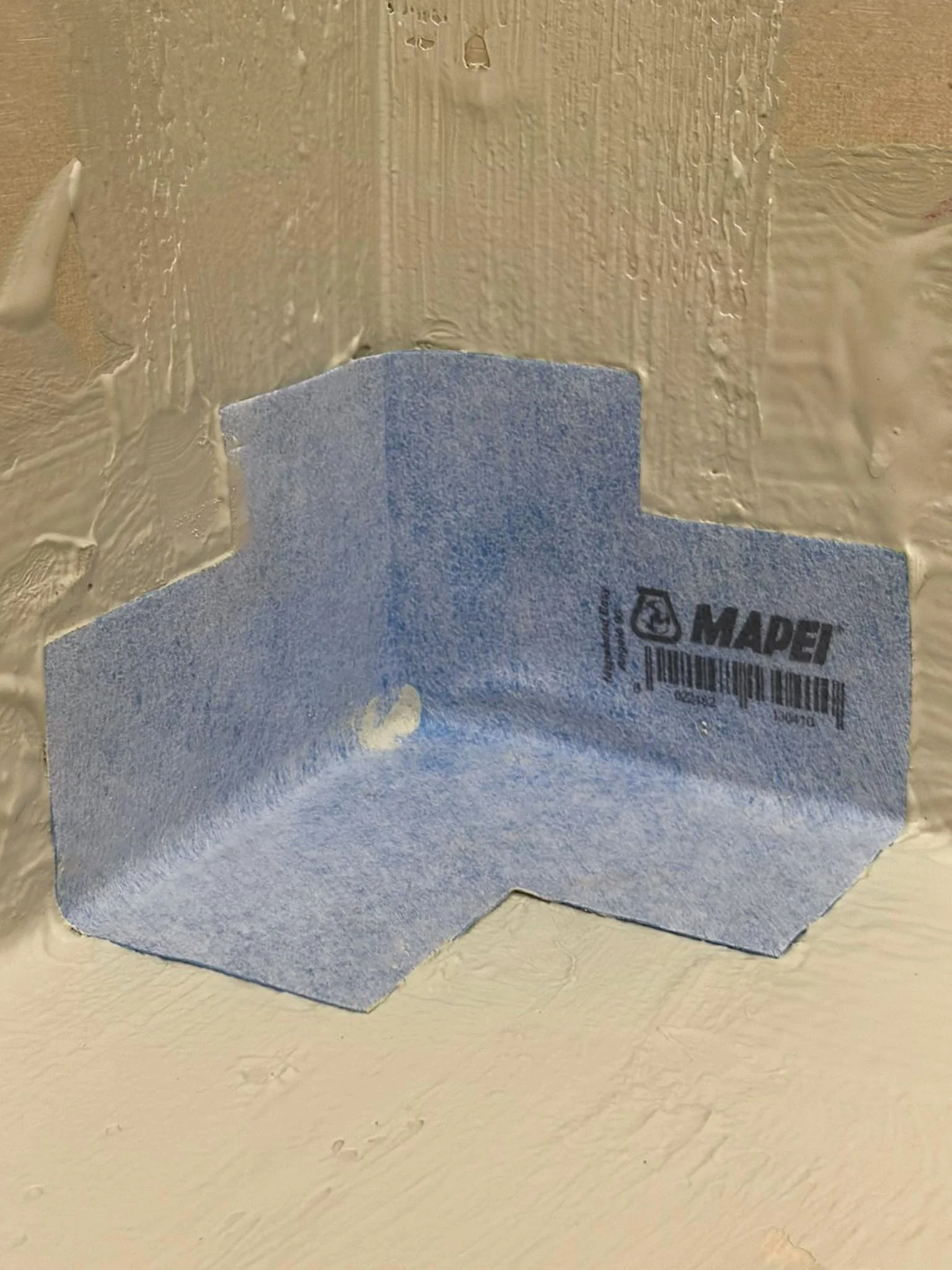 Blue painter's tape with the brand name 'MAPEI' adhered to a textured beige wall near the ceiling.
