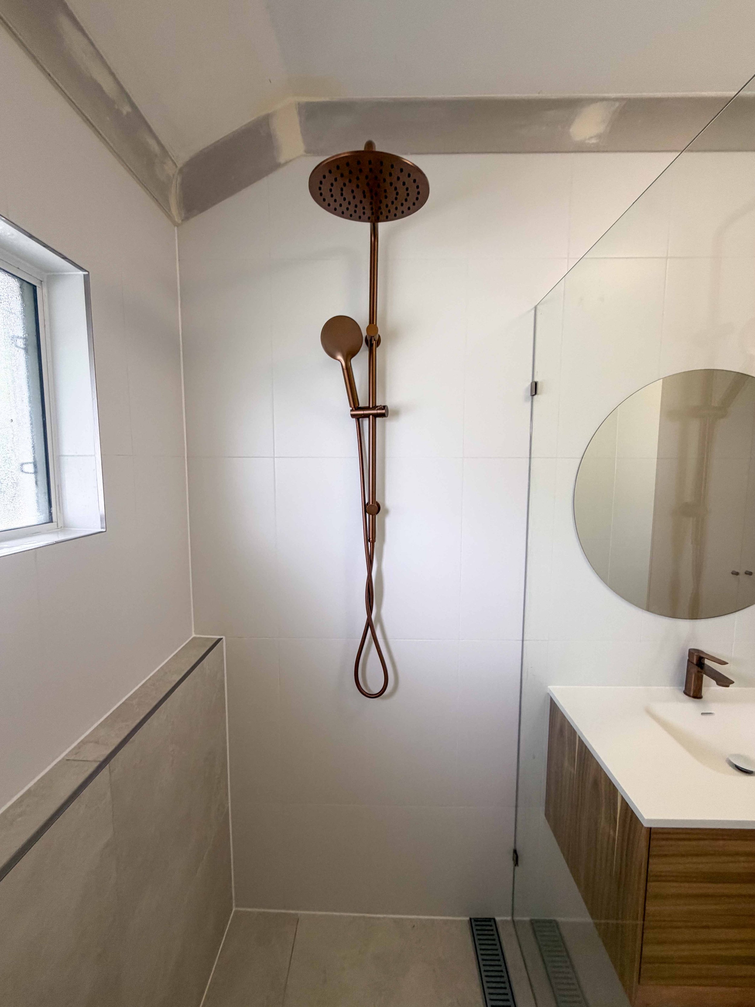 Modern walk-in shower renovation with a round rainfall showerhead, handheld shower, and white tiled walls in a bathroom in Cairns.