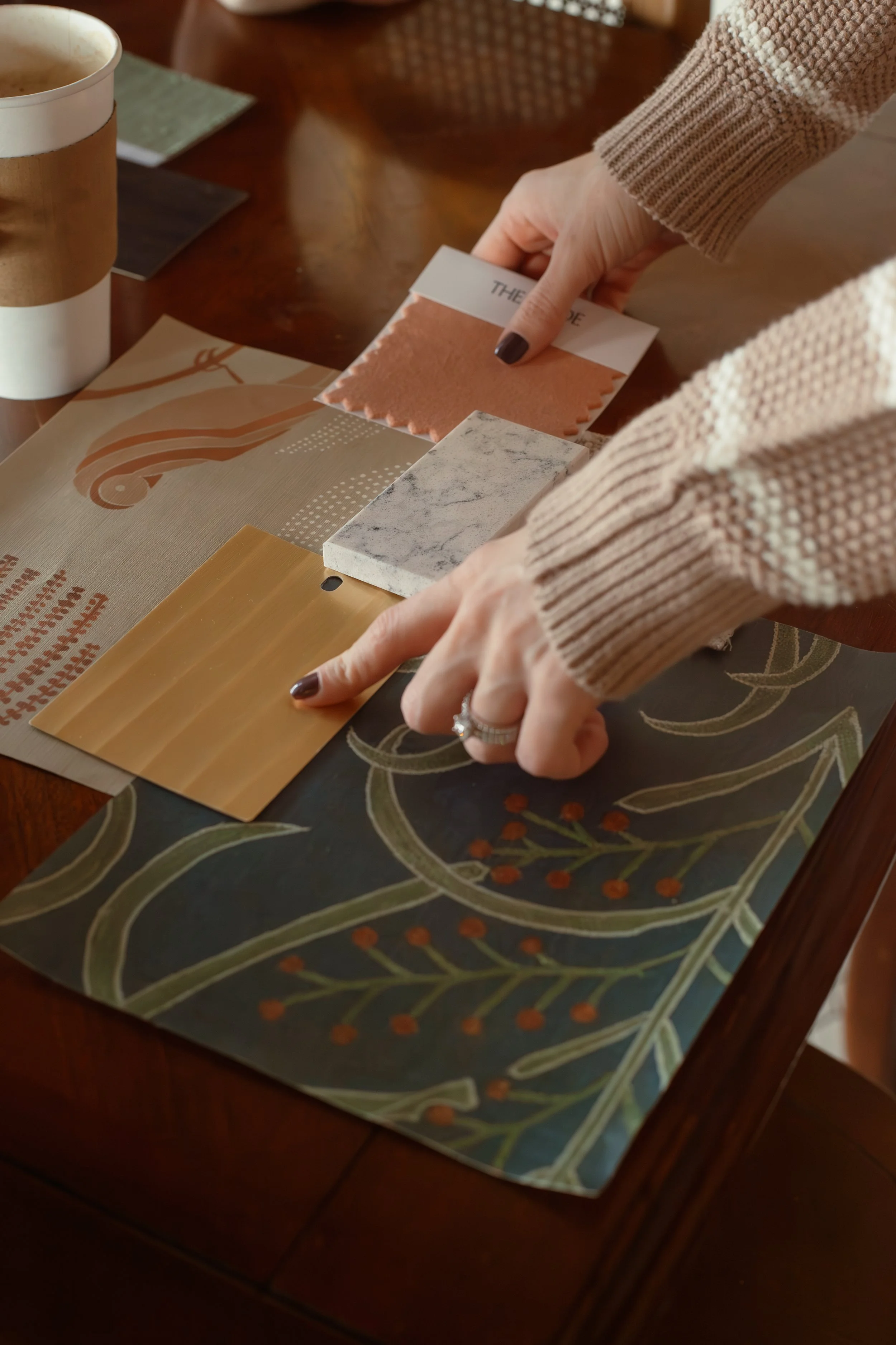 Person pointing at various fabric and wallpaper samples on a table.