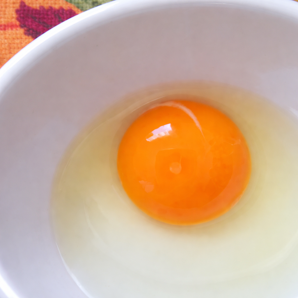 Close-up of a raw egg with an orange yolk in a white bowl.