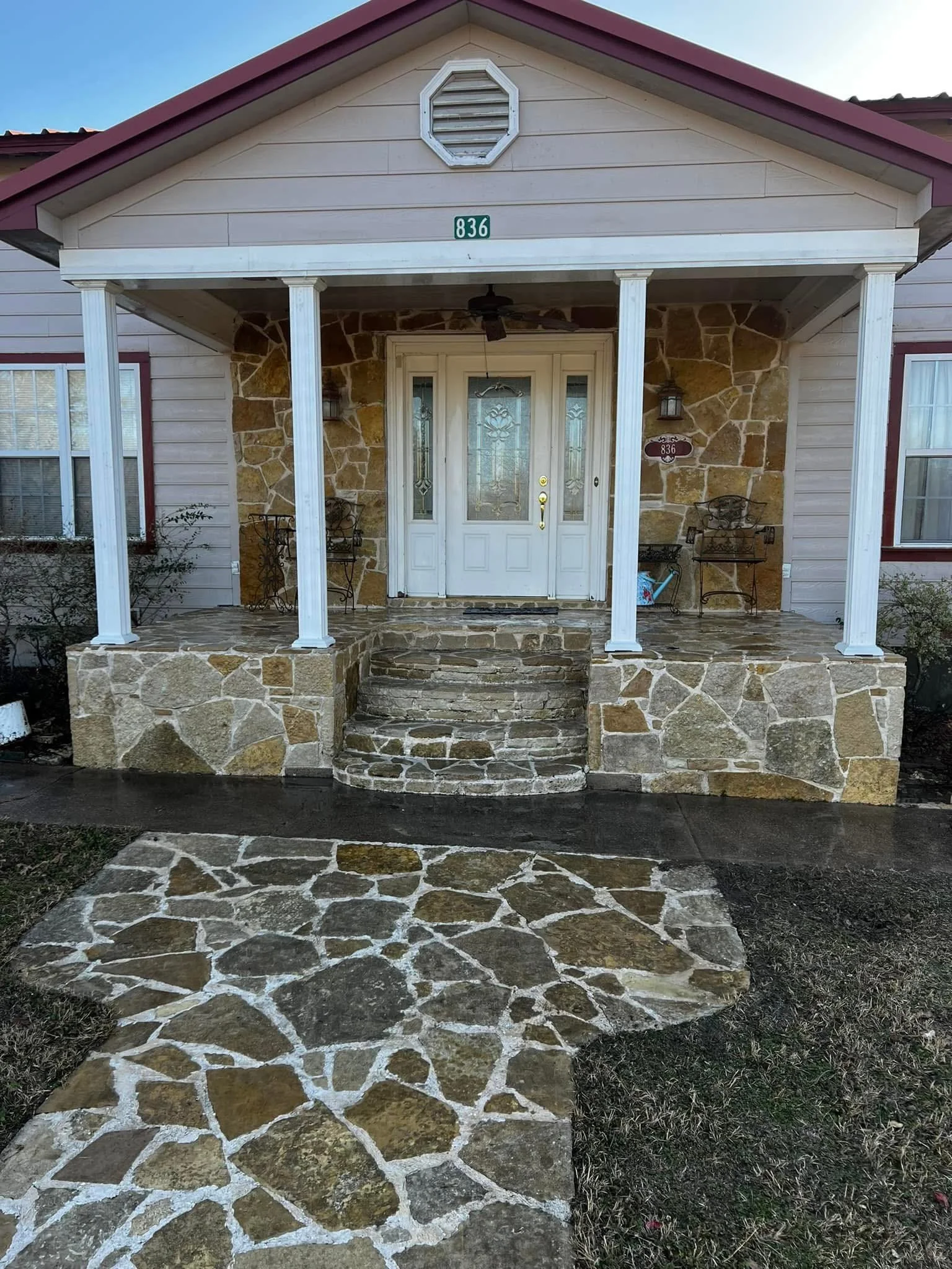 Front porch of a house with a stone walkway leading to the steps, stone porch floor, white front door with glass panels, and a covered roof supported by white columns. House number 836 displayed above the door.