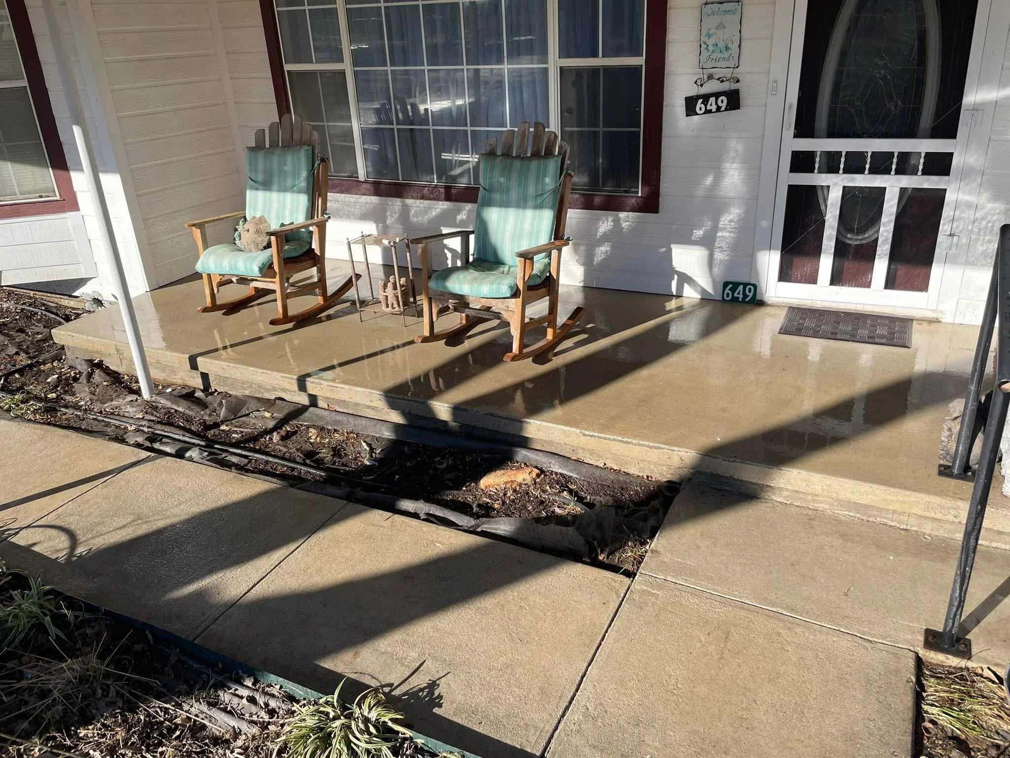 Front porch with two striped cushioned rocking chairs, a small table, and a welcome sign, with the house number 649 displayed, and a large window and screen door.