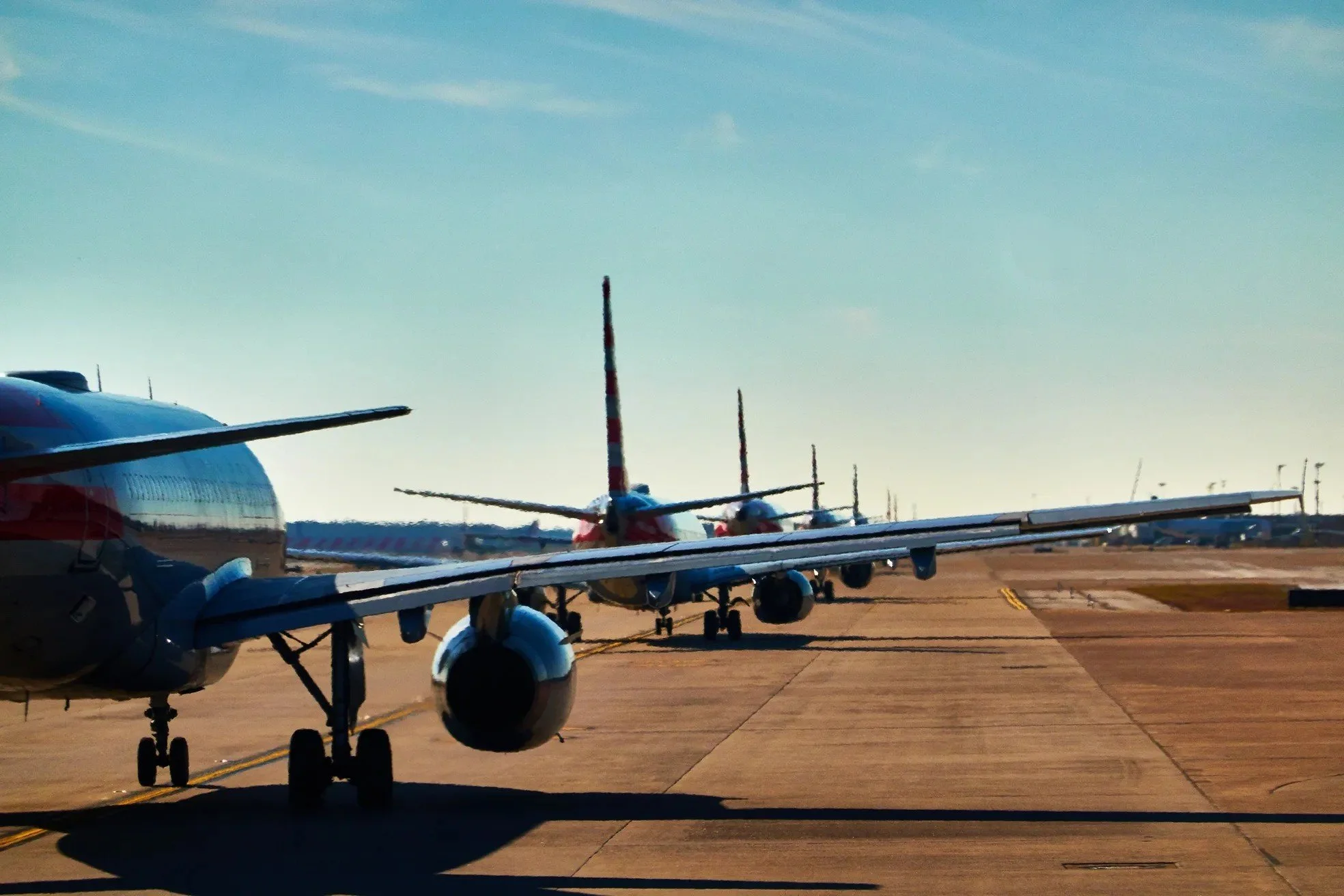 Multiple commercial airplanes parked on the tarmac at an airport during daylight, with clear skies.