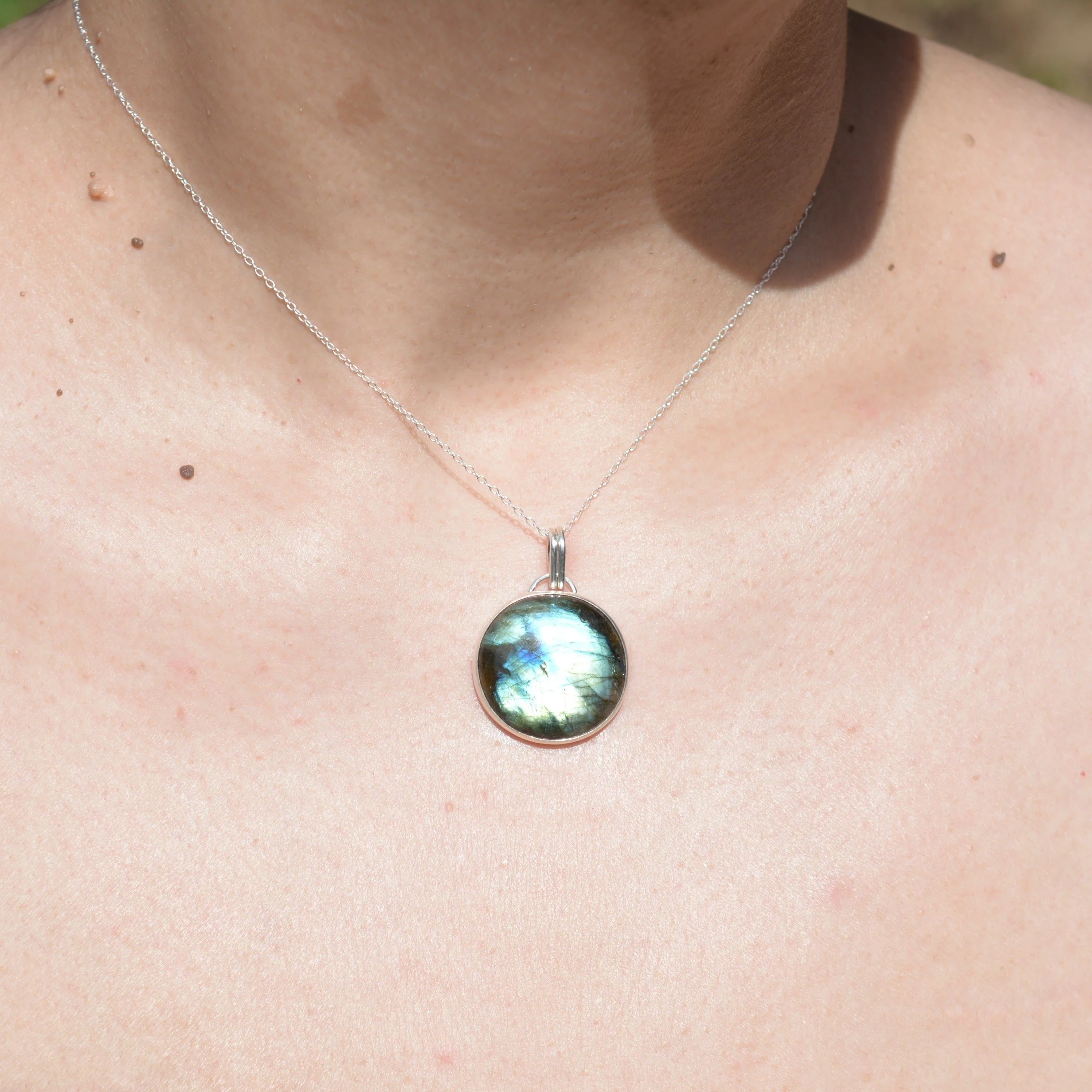 A close-up of a woman wearing a delicate silver chain necklace with a labradorite pendant.