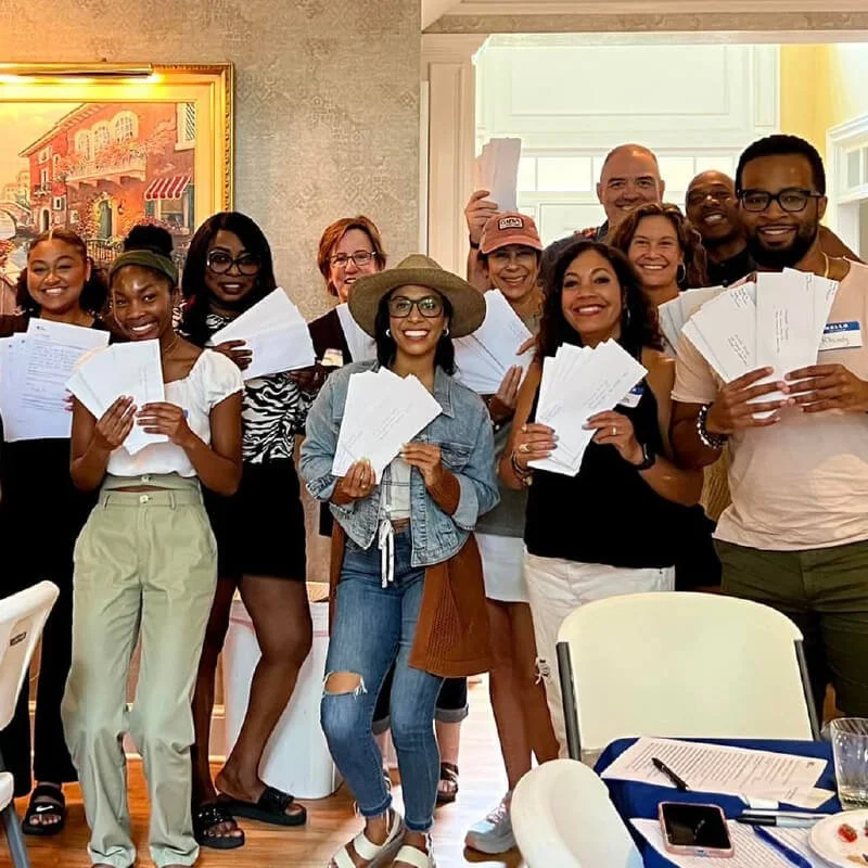 Group of volunteers smiling and holding handwritten Vote Forward letters in a room.