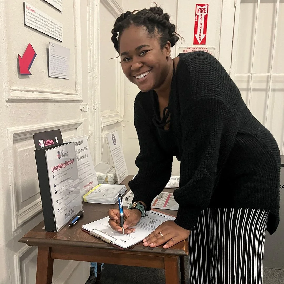 A woman with styled hair and a black sweater preparing a Vote Forward letter to send to voters.