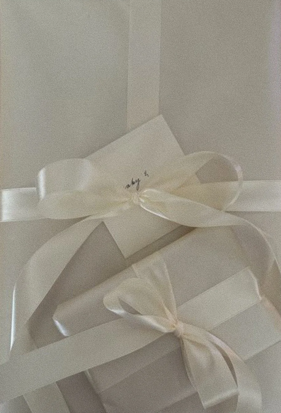 A white gift box decorated with a satin ribbon tied in a bow, with a small white card attached to the ribbon.