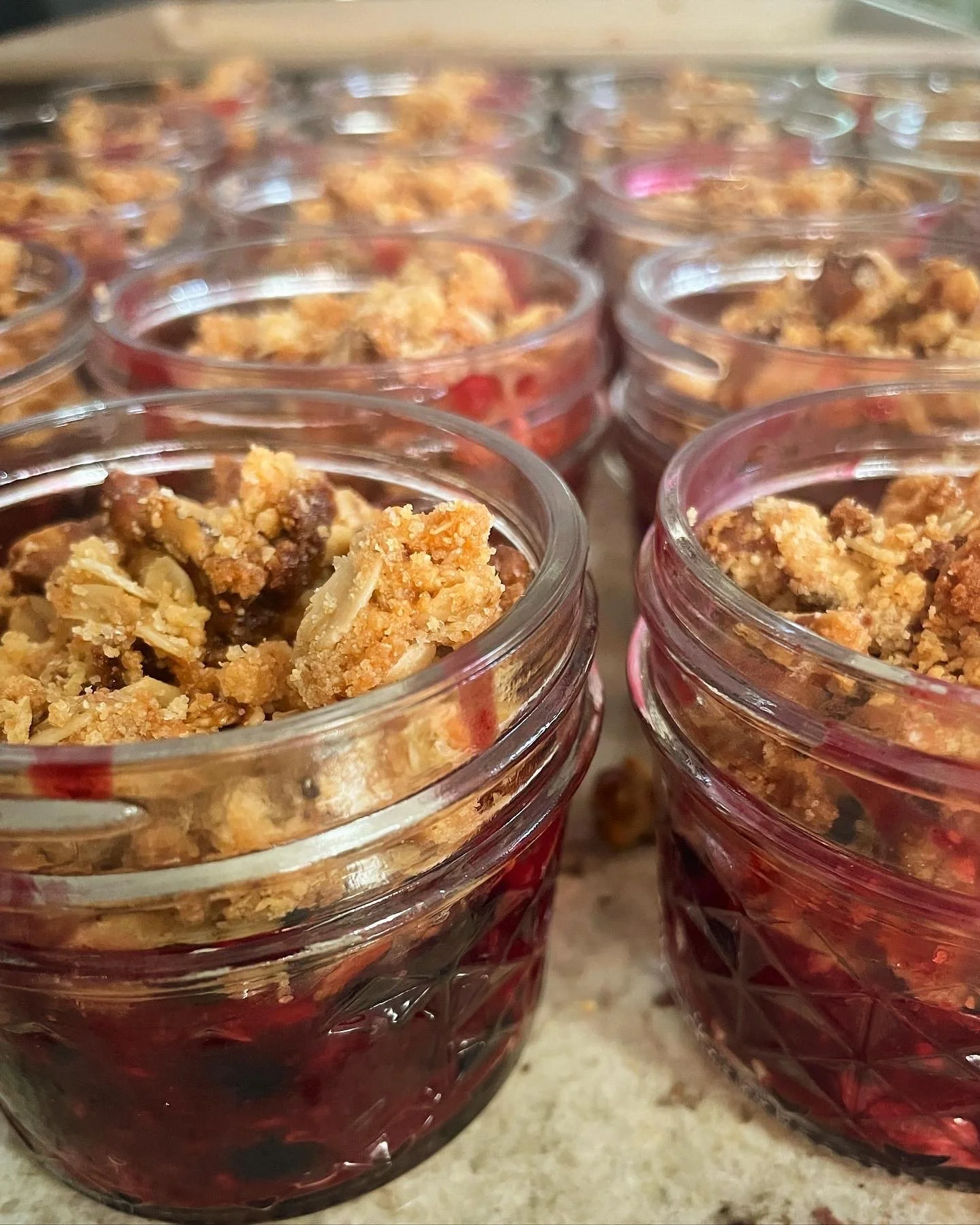 Multiple small glass jars filled with layered fruit crumble topped with oatmeal crumble, placed on a countertop.