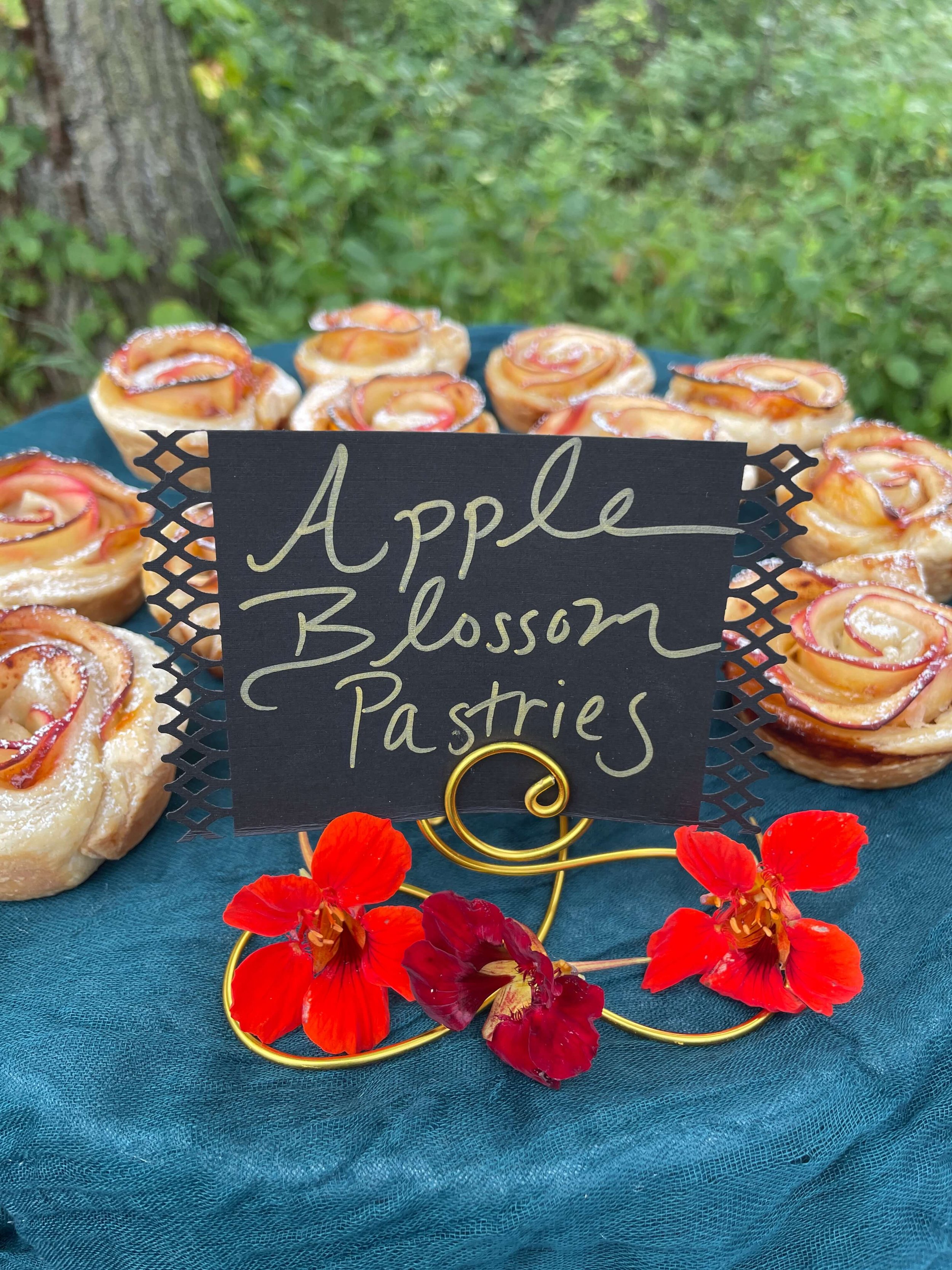 Apple blossom pastries displayed on a table with a sign reading 'Apple Blossom Pastries' and decorative red flowers.