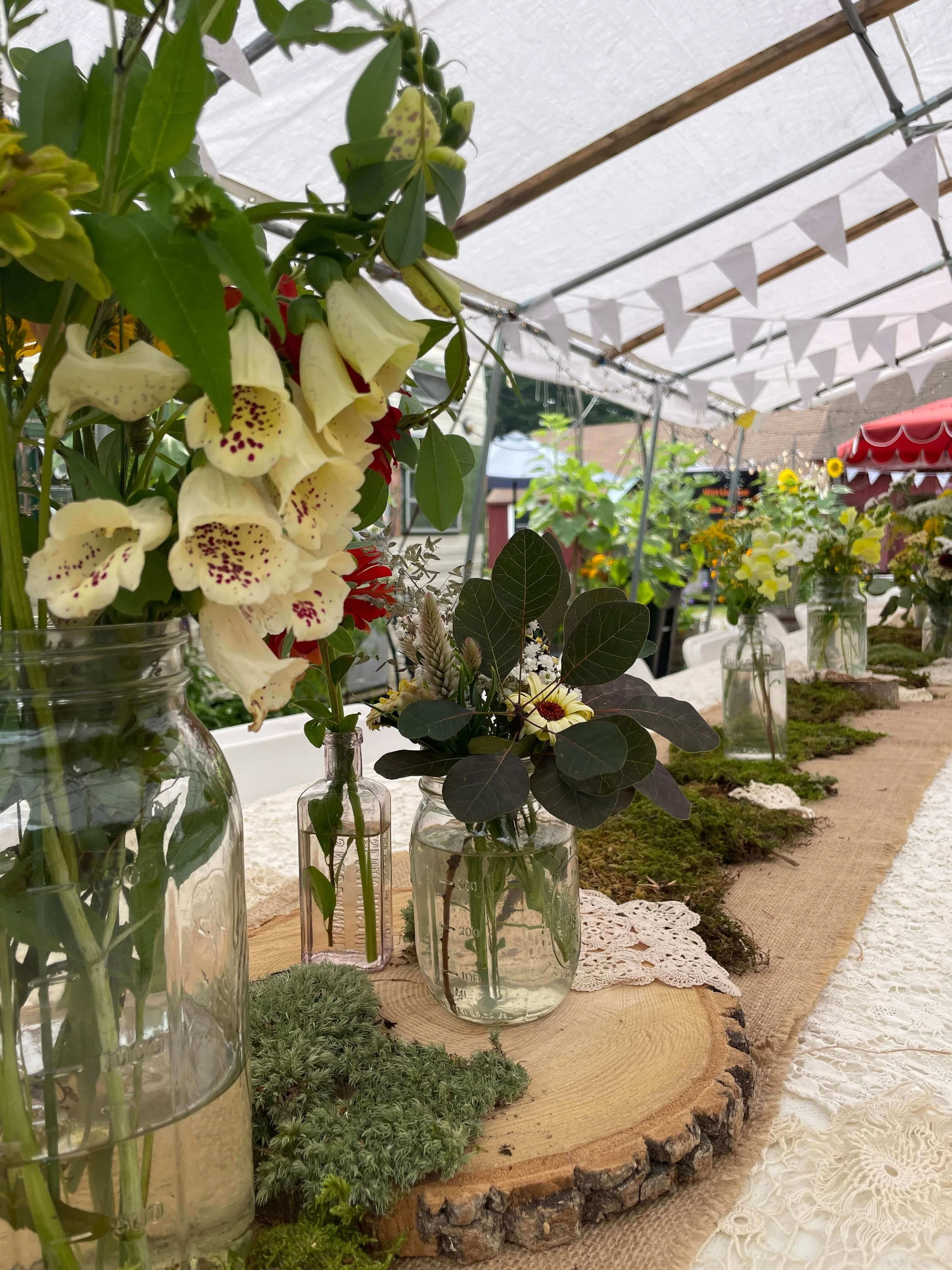 Vases with fresh flowers arranged on a rustic table under a tent at a wedding.