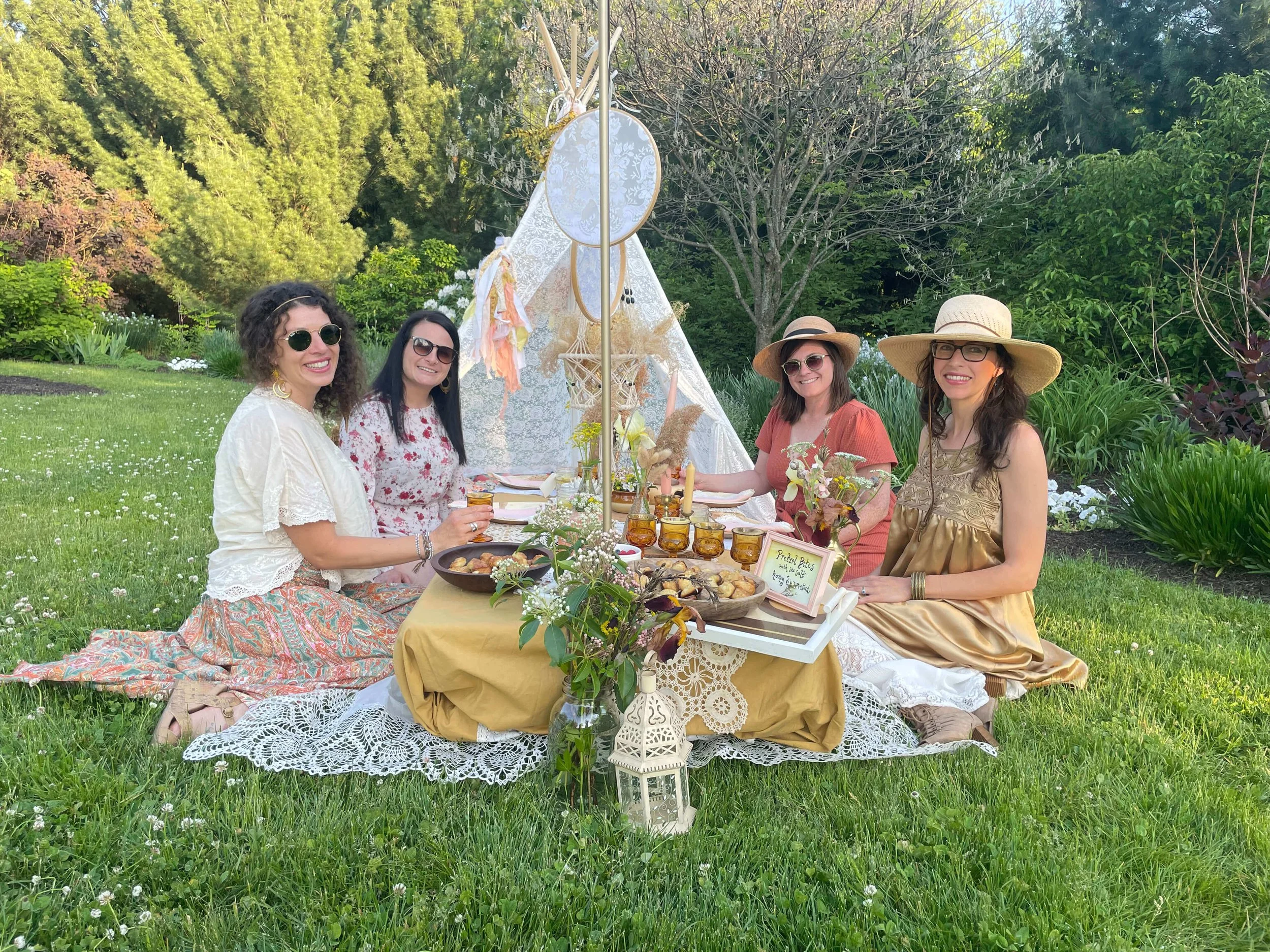Ladies sit around luxury picnic and lace tent in lawn