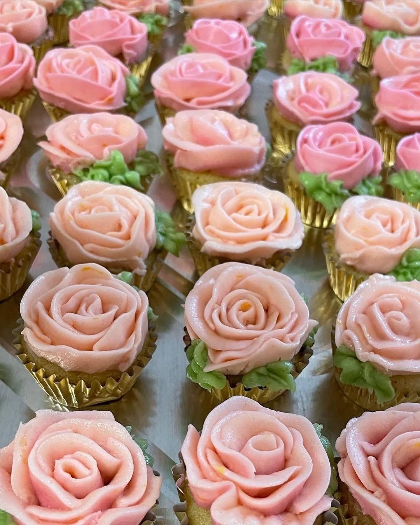 Cupcakes decorated with pink rose-shaped frosting and green leaves.