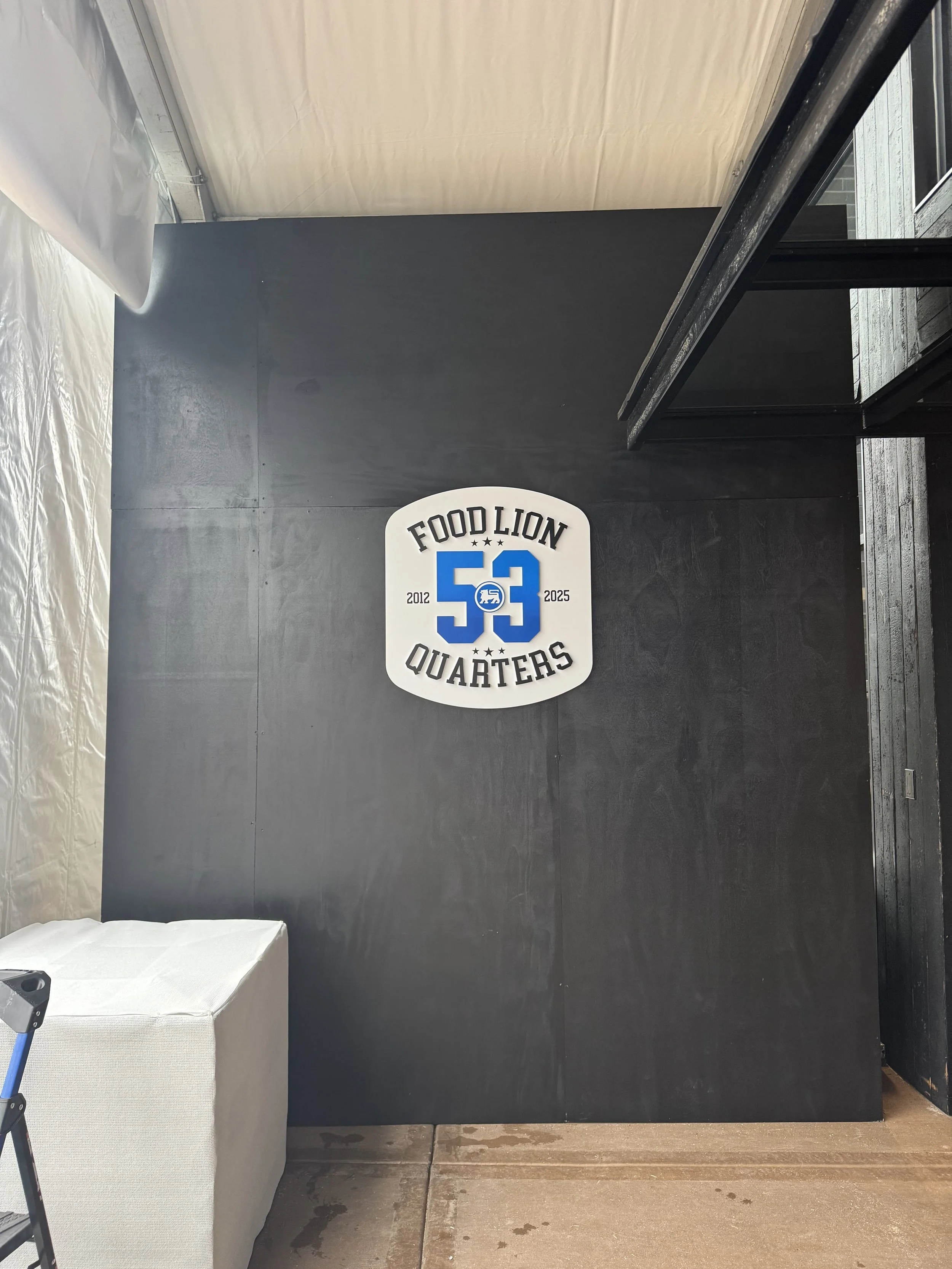 Wall sign reading 'Food Lion Quarters 53', with the years 2012 and 2025, and a logo of a lion inside a circle.