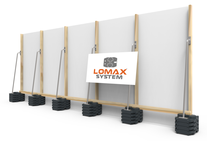A construction wall with the Lomax System logo displayed on a sign in front of it, supported by a series of sandbag bases.