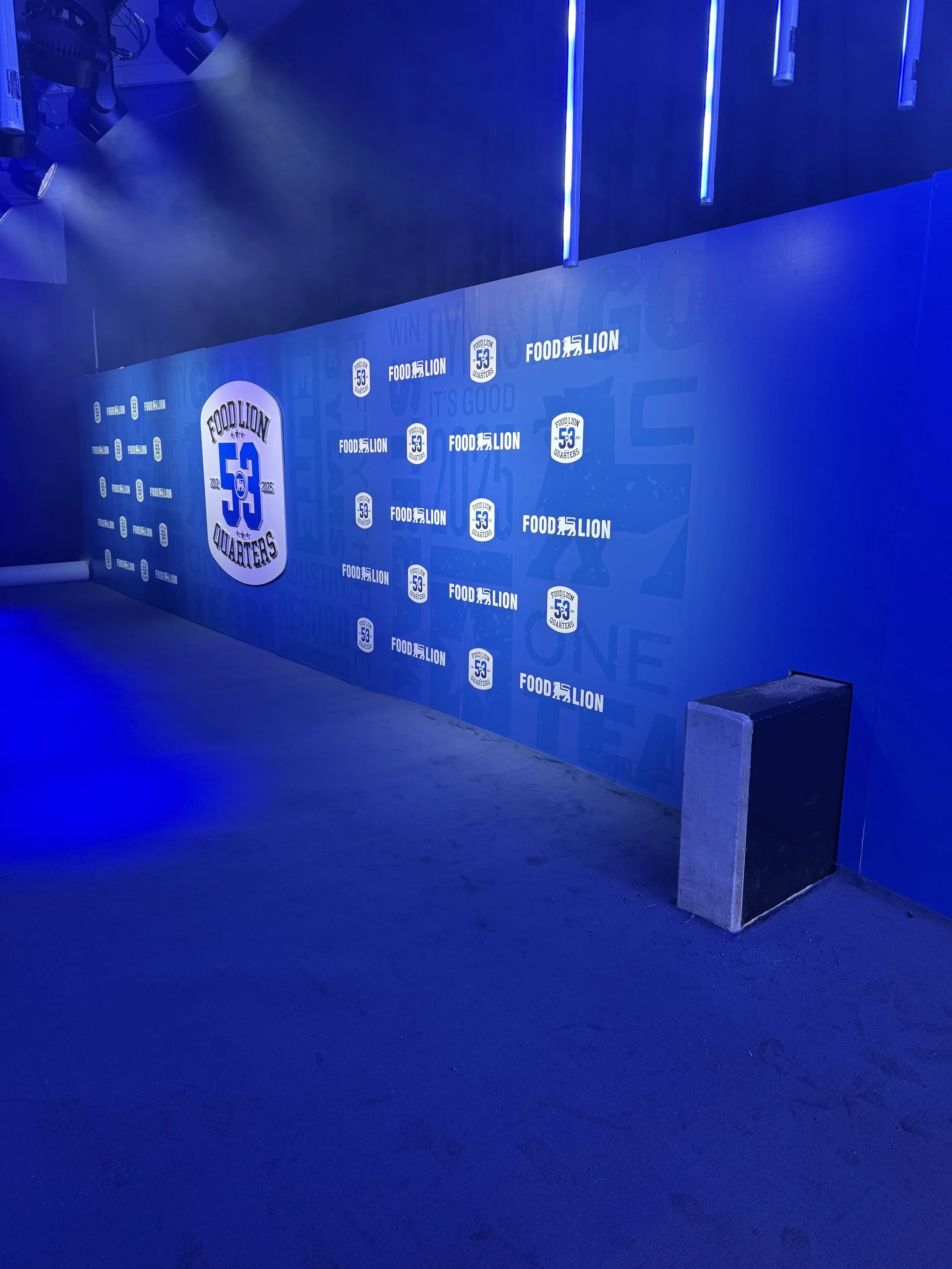 A blue event wall with logos and text celebrating Food Lion's 53rd anniversary, illuminated by blue lighting.