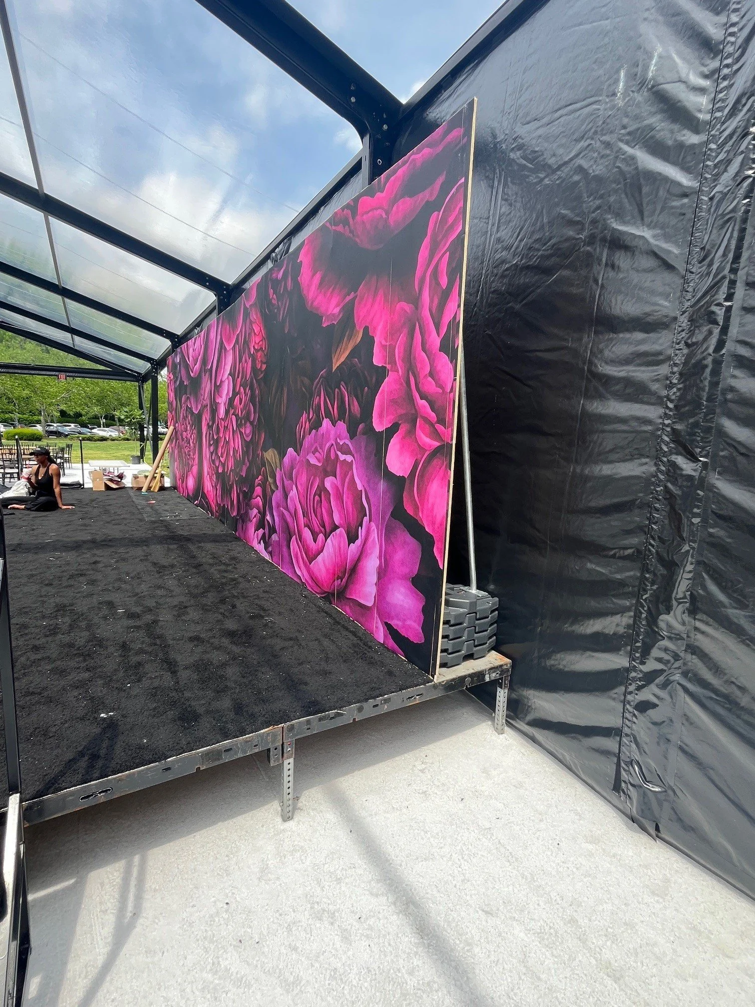Large canvas with pink and purple floral artwork on a black background, set up on a platform with a black plastic side wall and a transparent roof