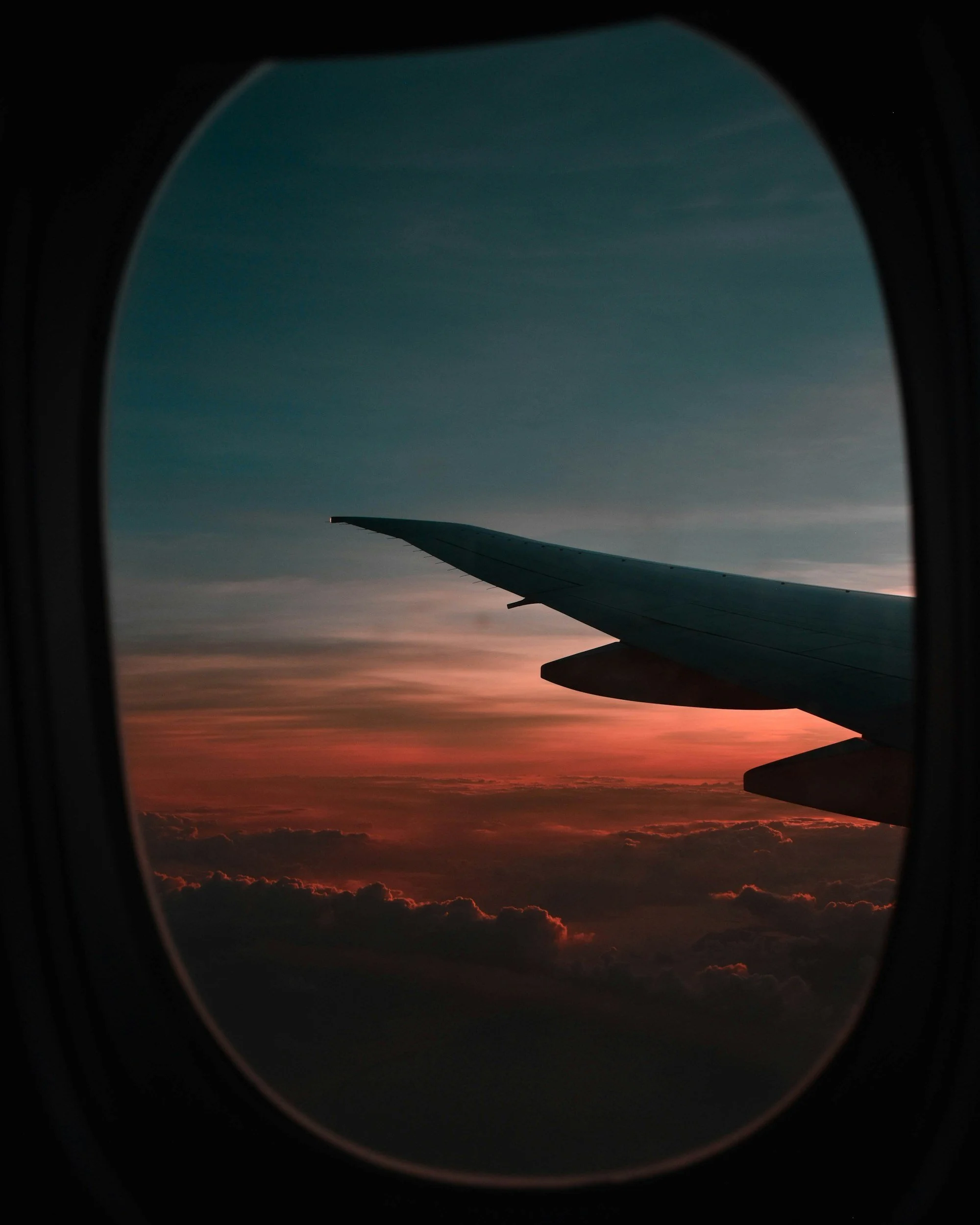 view of an airplane wing through an airplane window during sunset, with colorful clouds below