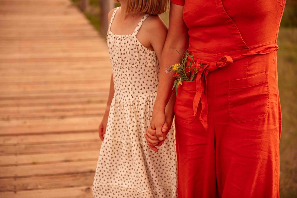 Mother holding hand of her daughter with wildflowers in her pocket