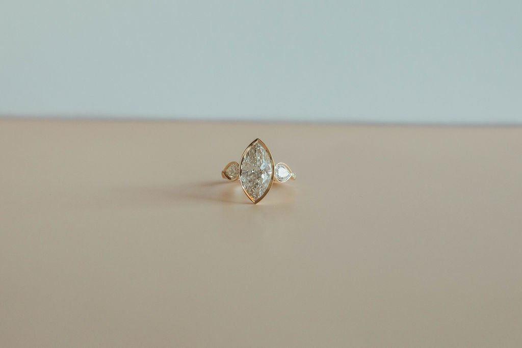 A diamond ring with a marquise-cut center stone and smaller side stones on a light-colored surface.