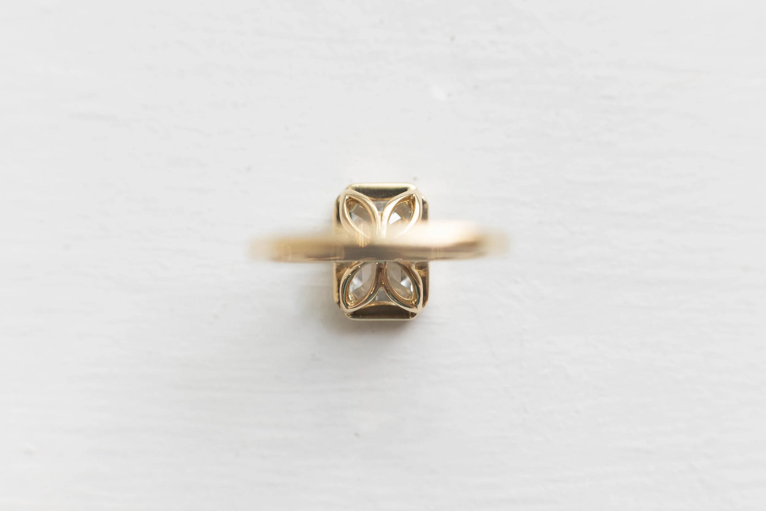 Close-up of a gold ring with a floral or leaf design on top, placed on a white surface.