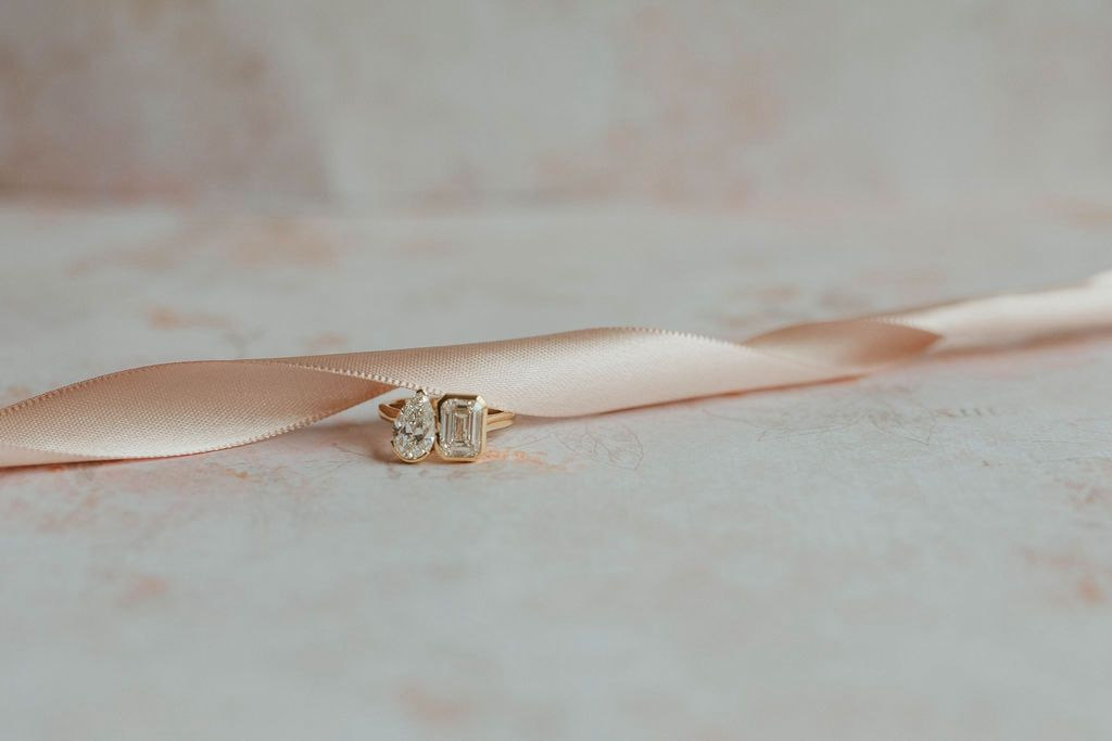 Diamond rings on a pink satin ribbon placed on a textured surface.