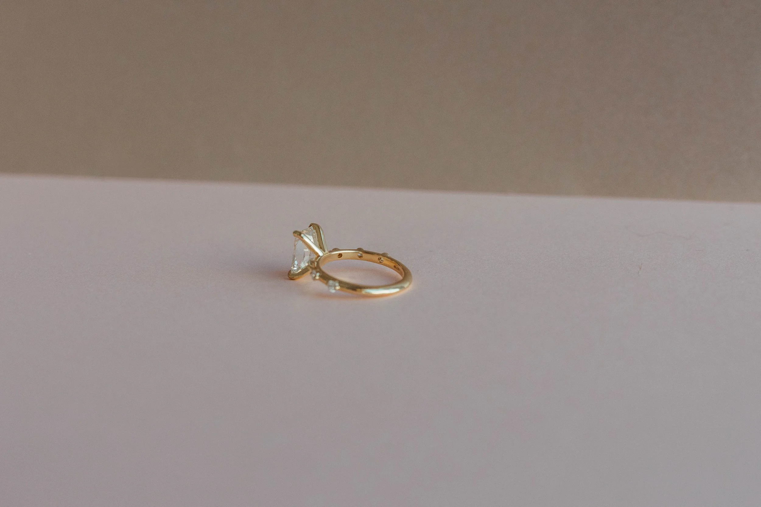 A gold ring with a large clear gemstone on a flat surface with a neutral background.