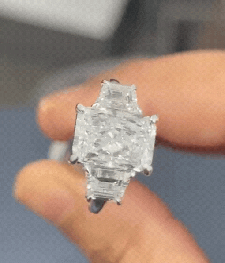 Close-up of a large, clear diamond ring held between fingers.