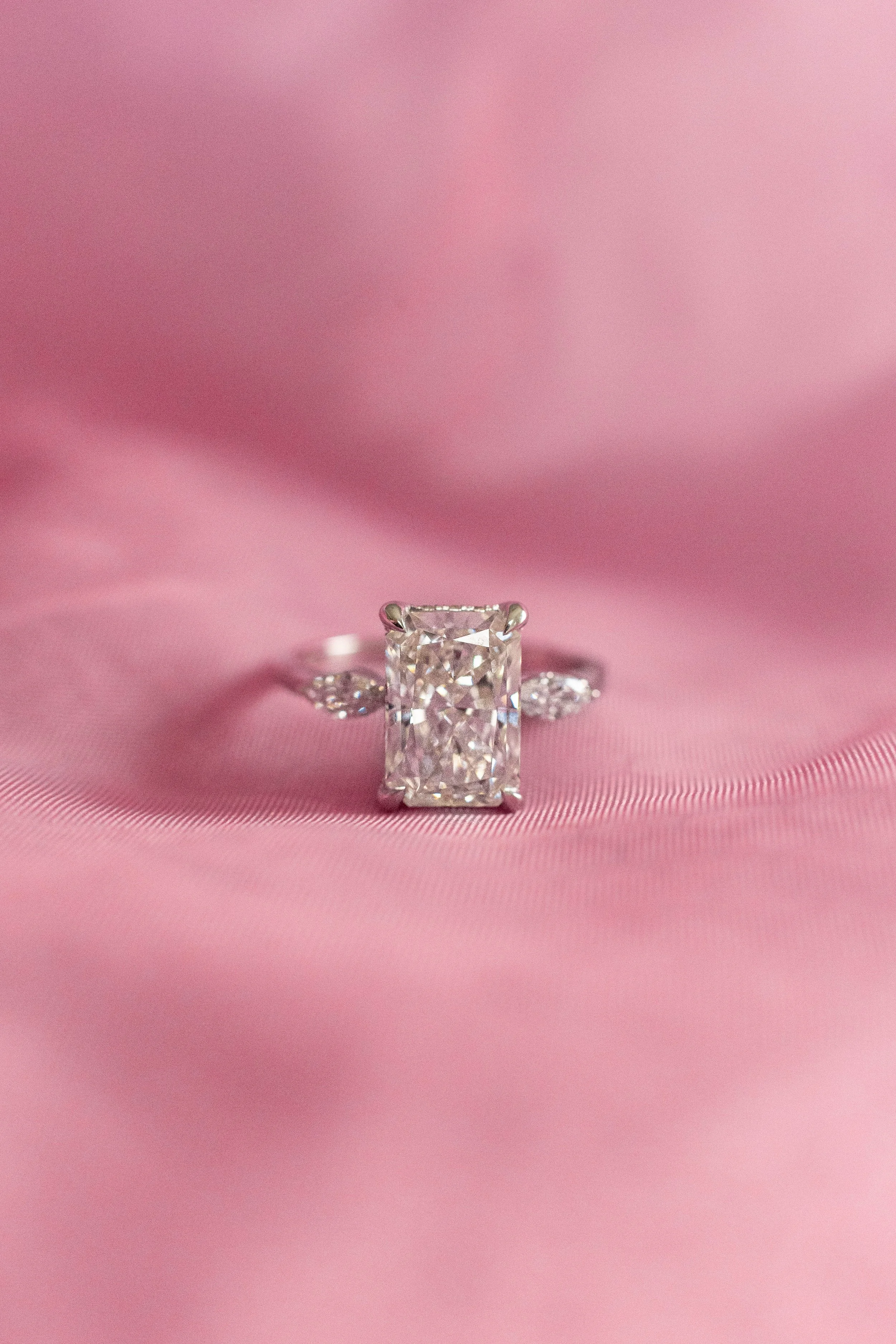 Close-up of a diamond ring with a large rectangular cut diamond, set against pink fabric.