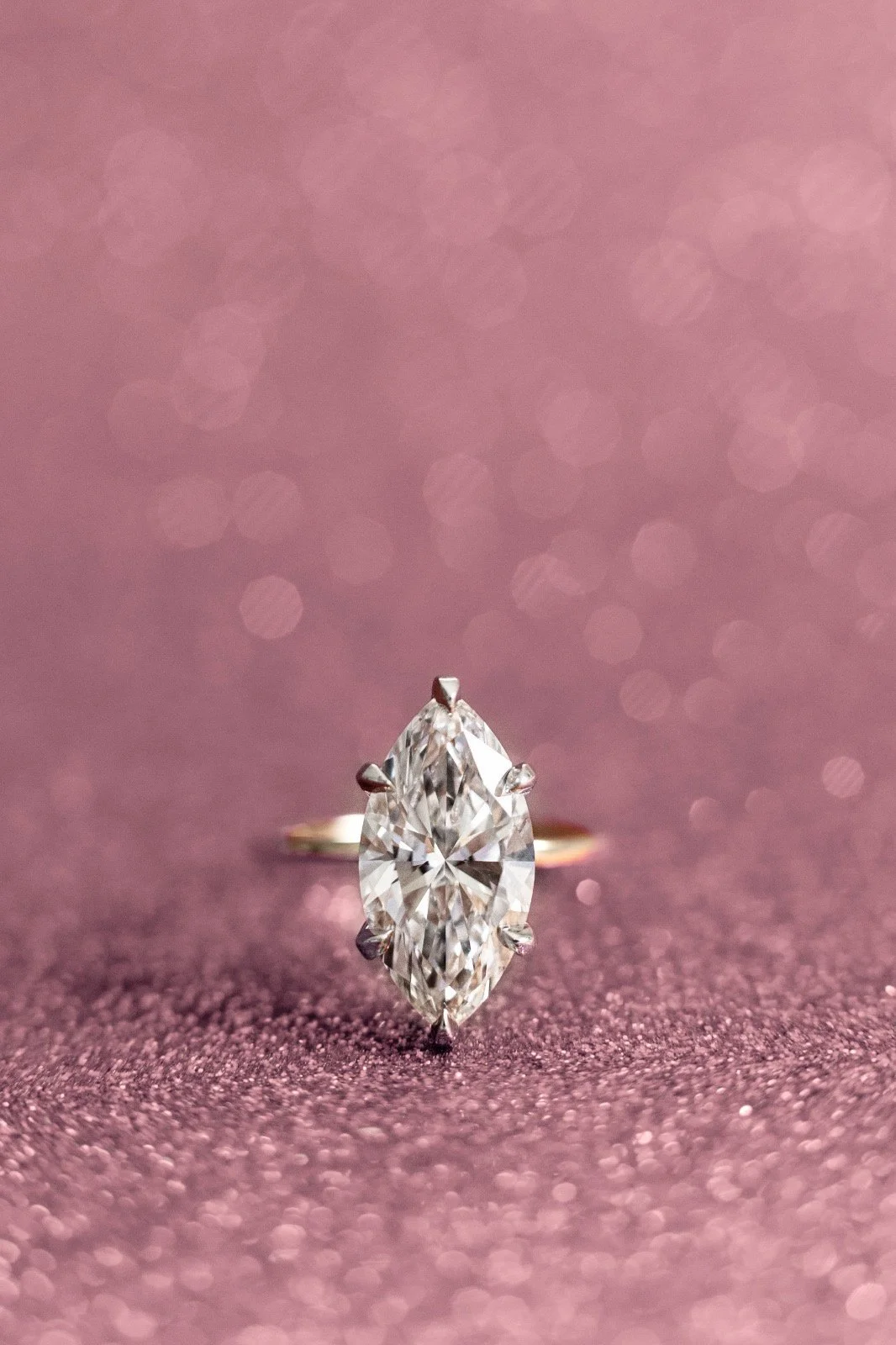 Close-up of a marquise-cut diamond ring on a pink, sparkly background.
