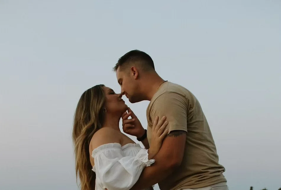 A couple sharing a romantic moment, about to kiss, outdoors during what appears to be dusk or dawn.