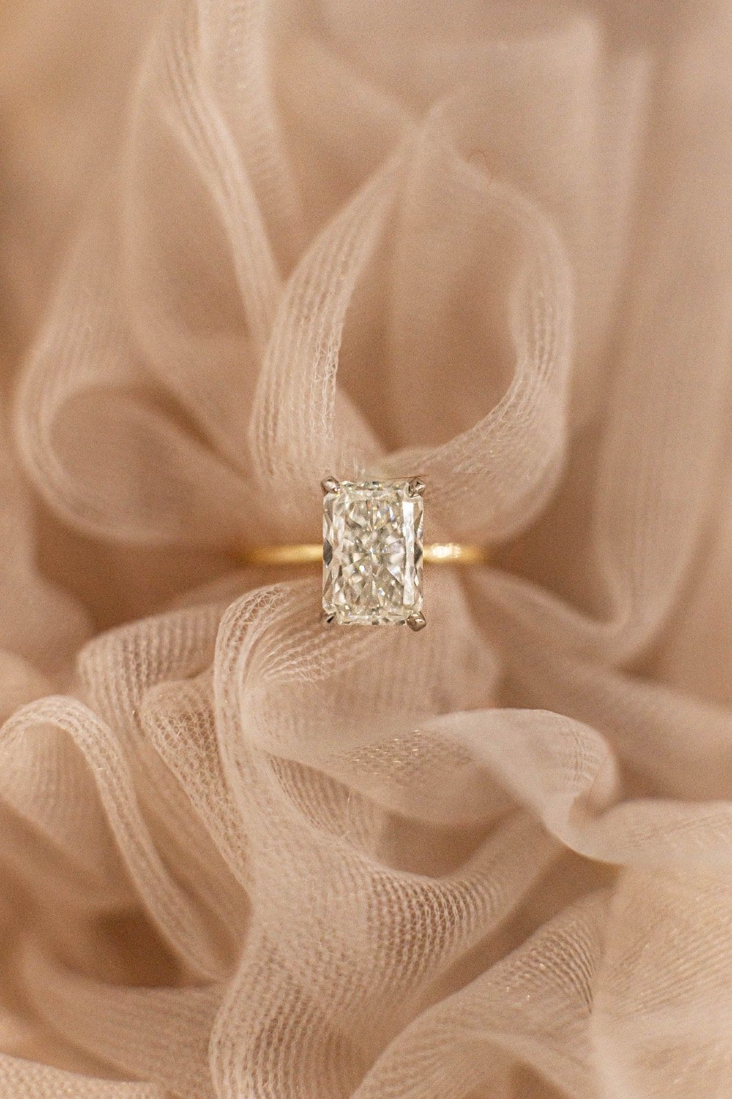 Close-up of a diamond ring with an emerald-cut diamond, resting on soft, cream-colored fabric with ruffled texture.