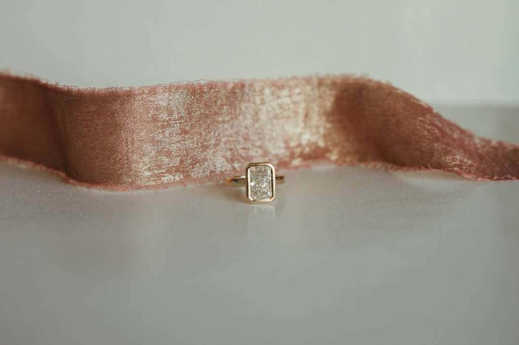A gold ring with a rectangular diamond setting placed on a soft pink velvet ribbon.