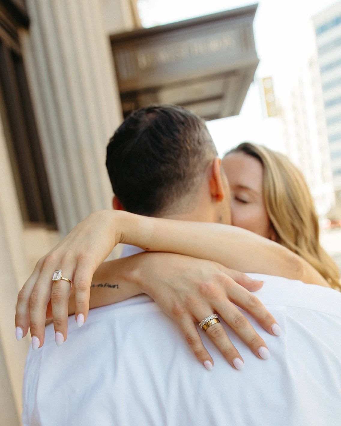 A couple embracing and kissing on a city street, with focus on their hands and rings.