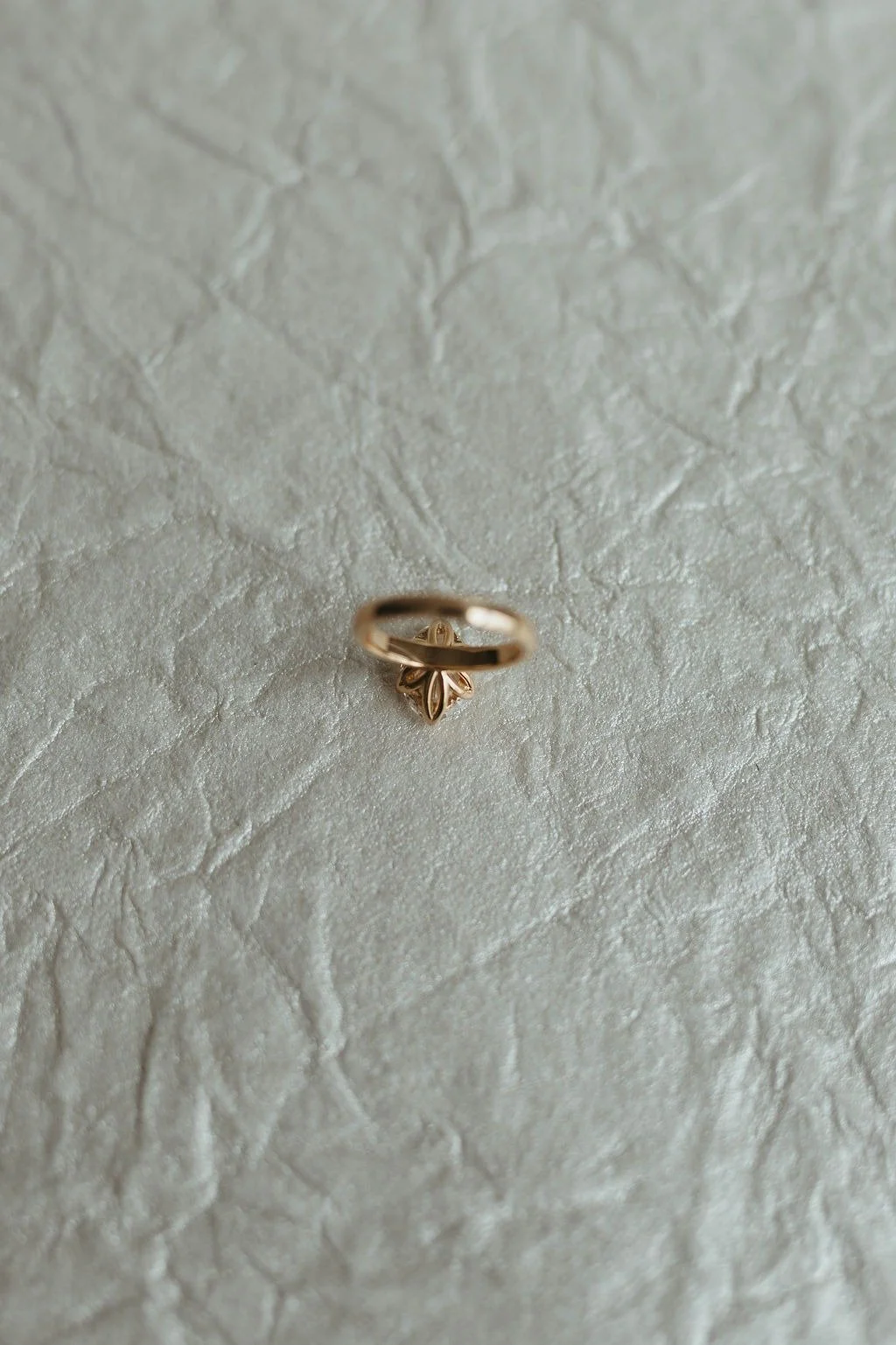 A gold ring with a small decorative element underneath, resting on a textured, light-colored surface.
