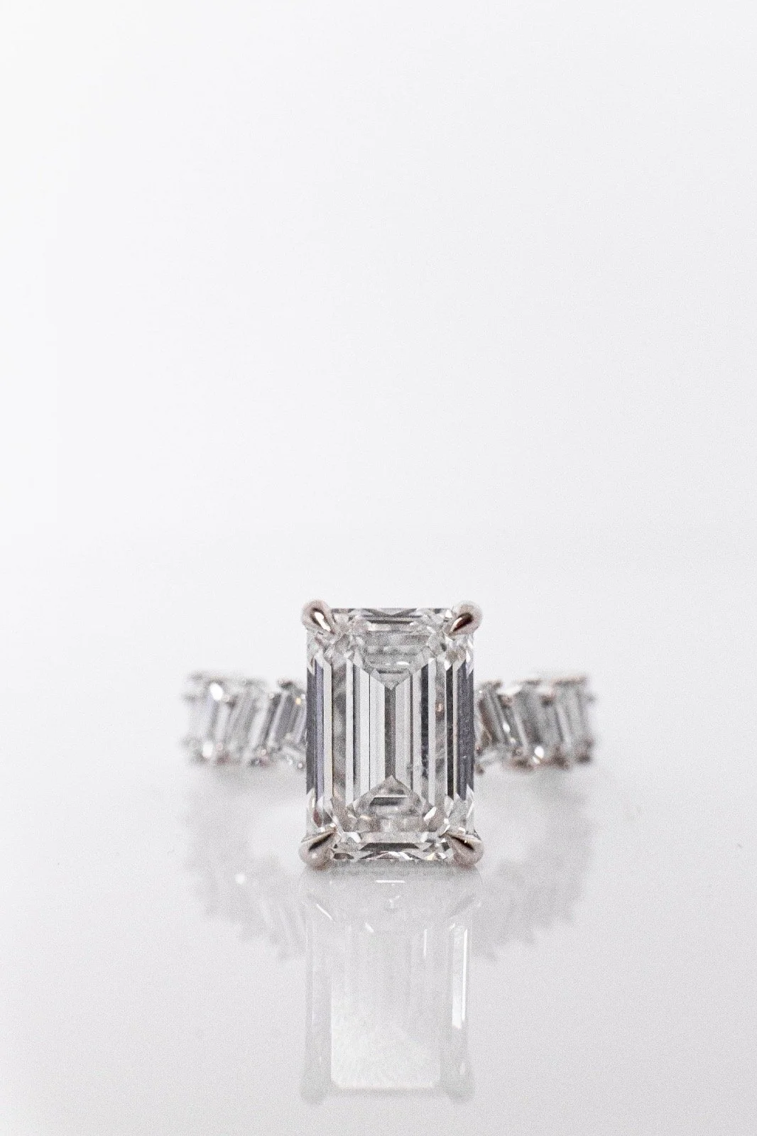 A diamond ring with a large emerald-cut diamond centerpiece and a band made of smaller diamonds, set in white gold or platinum, photographed on a reflective surface.