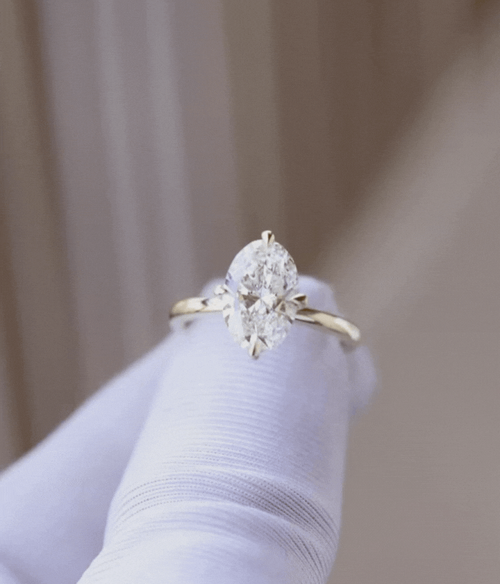 Close-up of a gold ring with an oval-shaped diamond, held on a white glove.